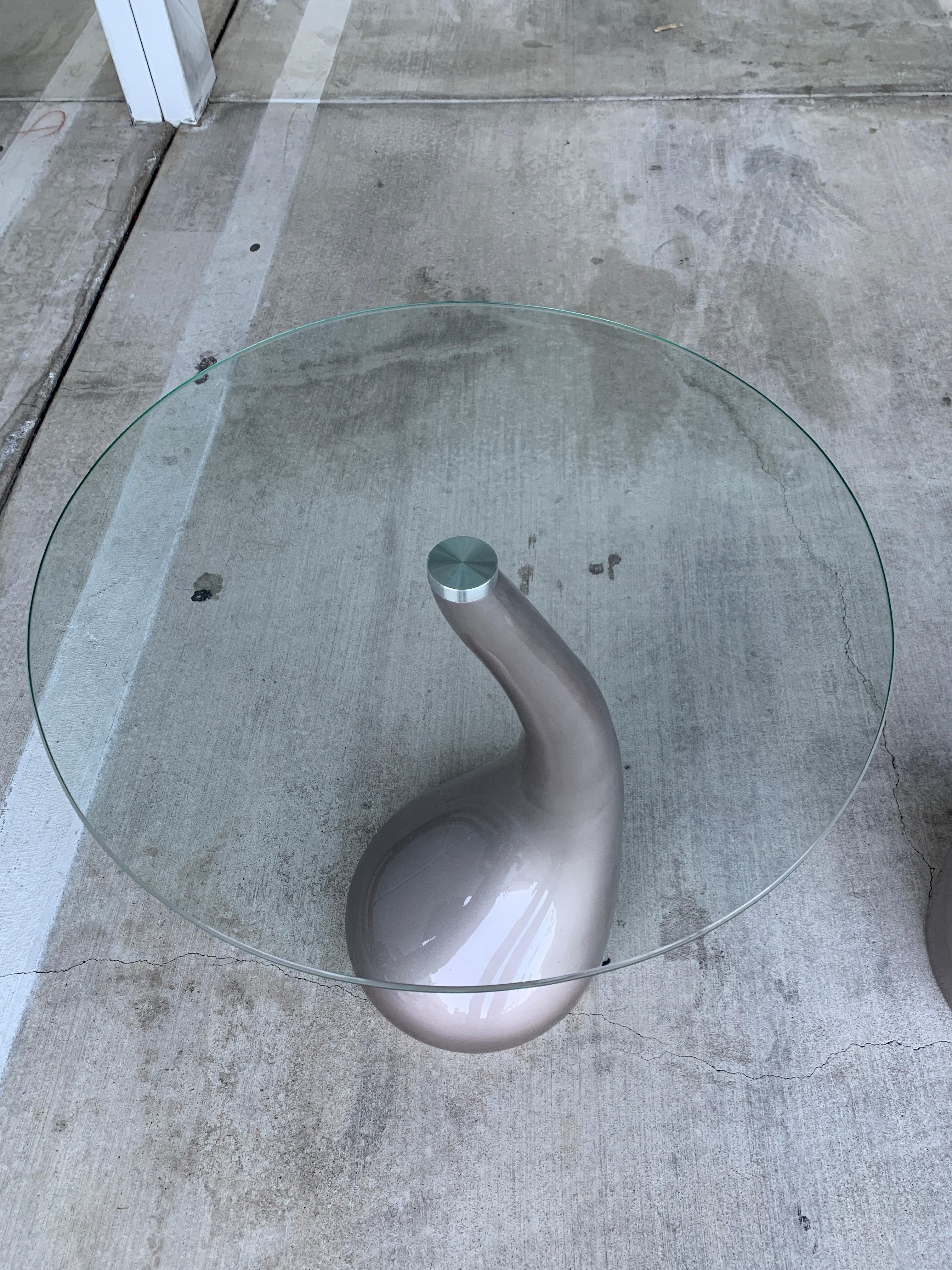 A pair of sinuous resin base tables with round glass tops. These tables came from a Movie Prop supply house. The top glass screws on to the base. We have has the bases re-painted in a glossy pewter silver color. The glass tops have some minor marks