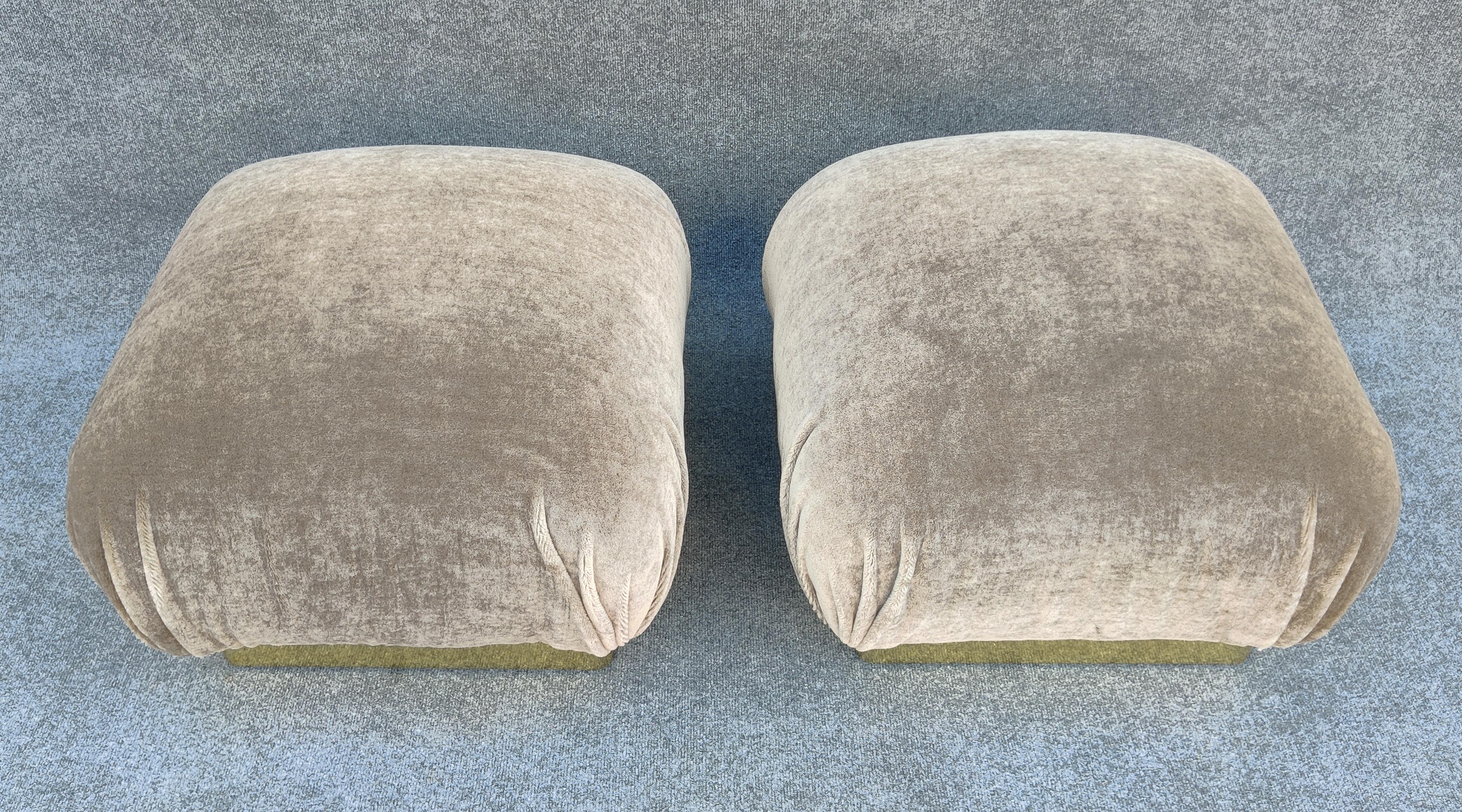 This pair of poufs or ottomans were made in the 1980s after the design was made iconic by Karl Springer. On a base of brass plated sheet metal over a wooden frame, this pair has been newly reupholstered in Maharam's 