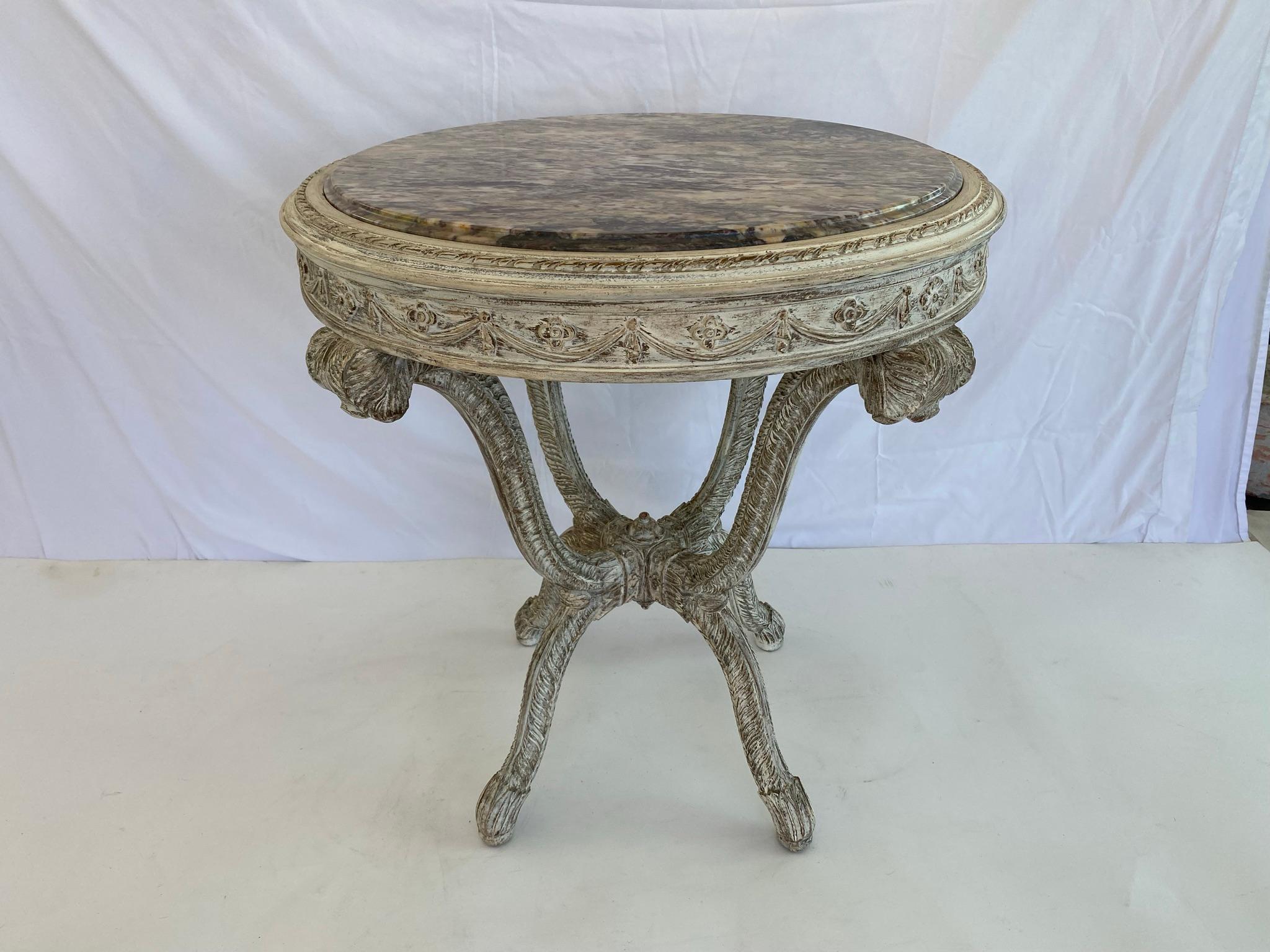 Pair of end tables, by Grosfeld House, both with a painted finish showing natural wear; each table having a round top of rouge marble, bordered by a gadrooned frame, over the apron carved with swags and quatrefoils, raised on four, splayed legs,