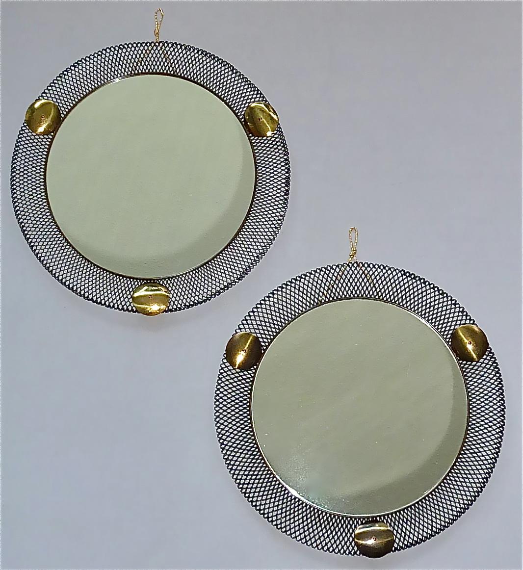 Rare pair of round midcentury wall mirrors which are made in the style of Jacques Biny, Mathieu Mategot or Pierre Guariche, France or Italy circa 1955. They are made of black lacquered or enameled stretched metal, lovely patinated brass details,