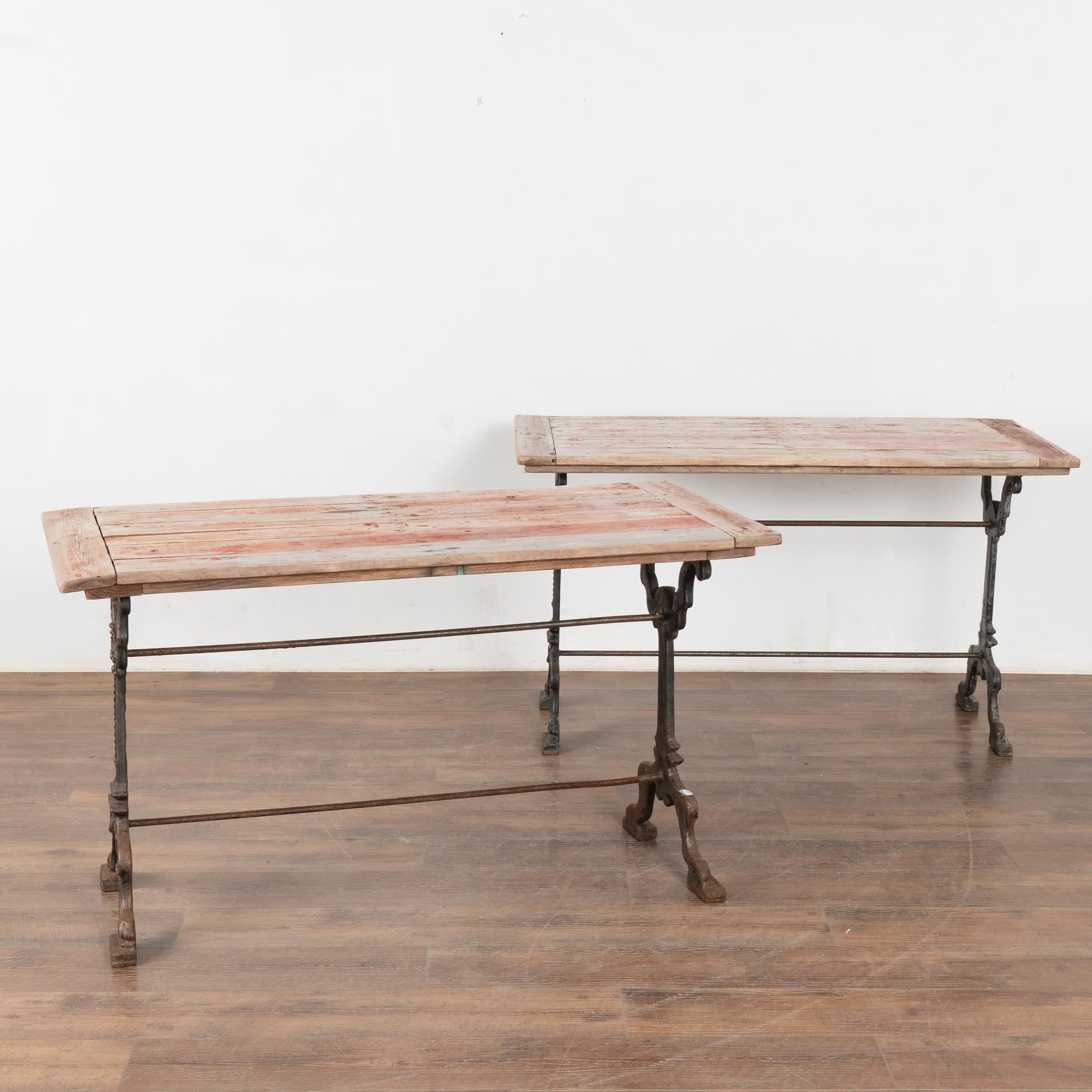 Cette paire de tables d'appoint rustiques a des bases en fer ancien qui complètent la patine usée et vieillie des plateaux en pin. Des restes de peinture rouge et de légères touches de vert sont encore visibles sur le dessus, ce qui indique qu'ils