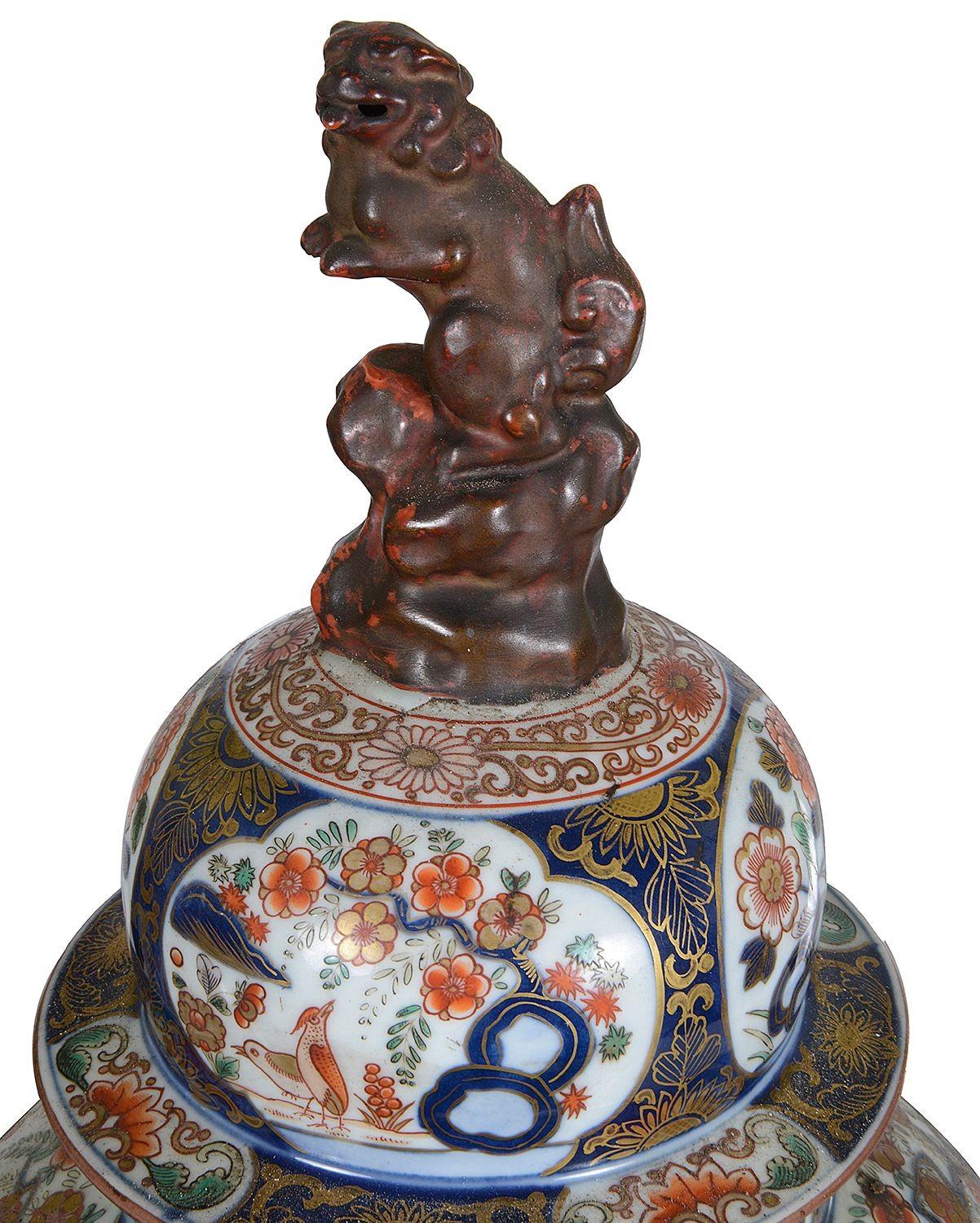 A handsome pair of Samson porcelain lidded vases in the style of 18th Century Japanese Arita Imari. Each with Terracotta Foo dog finials, inset hand painted panels depicting exotic birds, blossom trees and chrysanthemums with a cobalt blue ground.