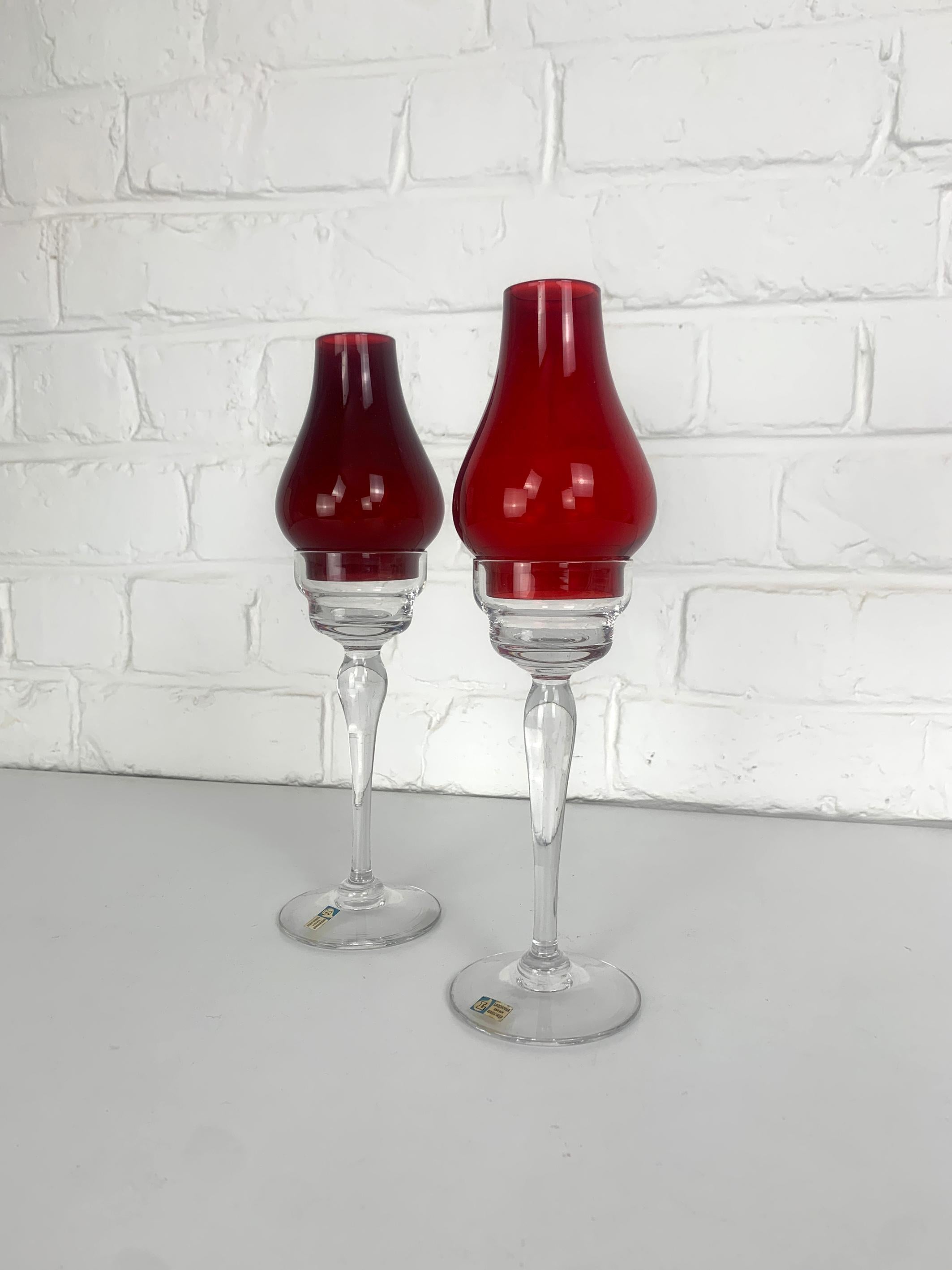 Pair of Swedish Modernist candelabra by Gunnar Ander. Produced by Lindshammar Glasbruk in Sweden. 

The base of the candle-holders in clear glass, the shades in red glass (the red is slightly between the two).

The original labels stating