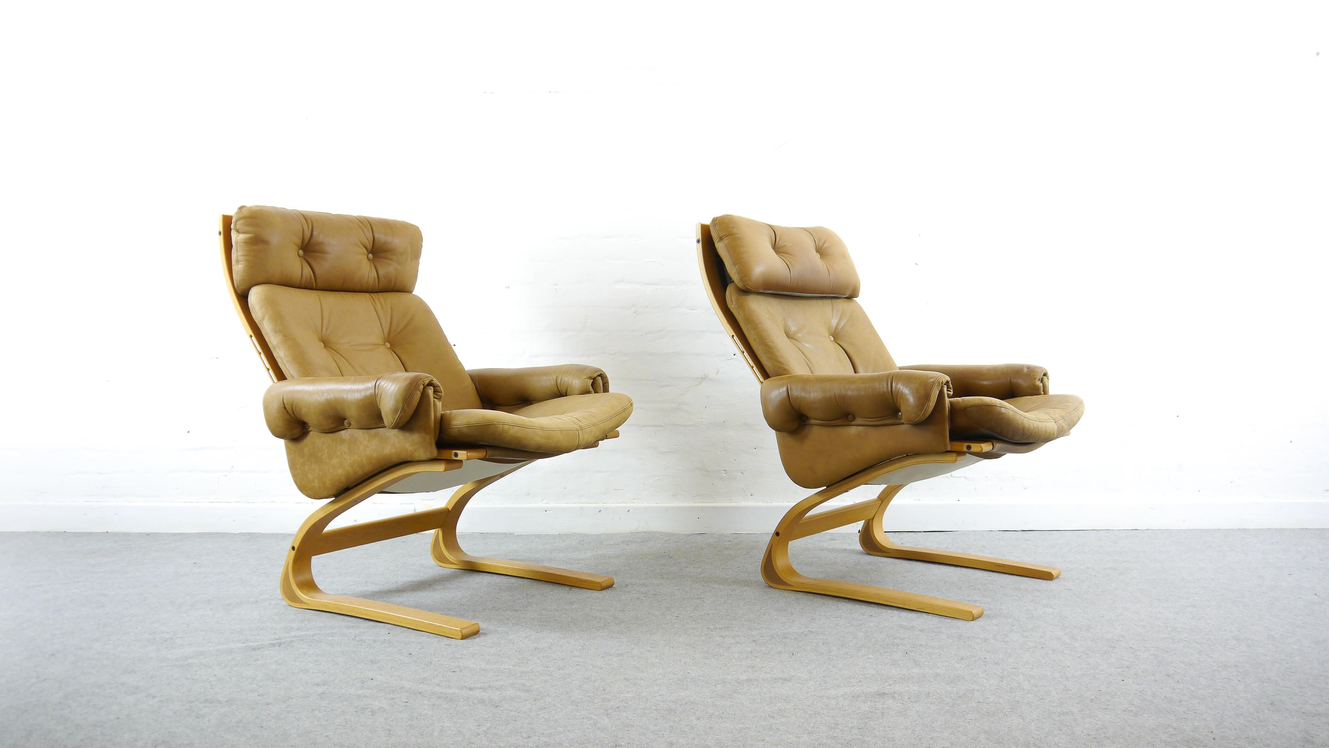 Paar (2) Kengu Lounge Chairs mit hoher Rückenlehne von Elsa und Nordahl Solheim. Hergestellt von Rybo Rykken & Co. in Norwegen, 1970er Jahre. Gepolstert mit original braunem oder karamellfarbenem Leder. Freitragende Konstruktion aus Holz mit
