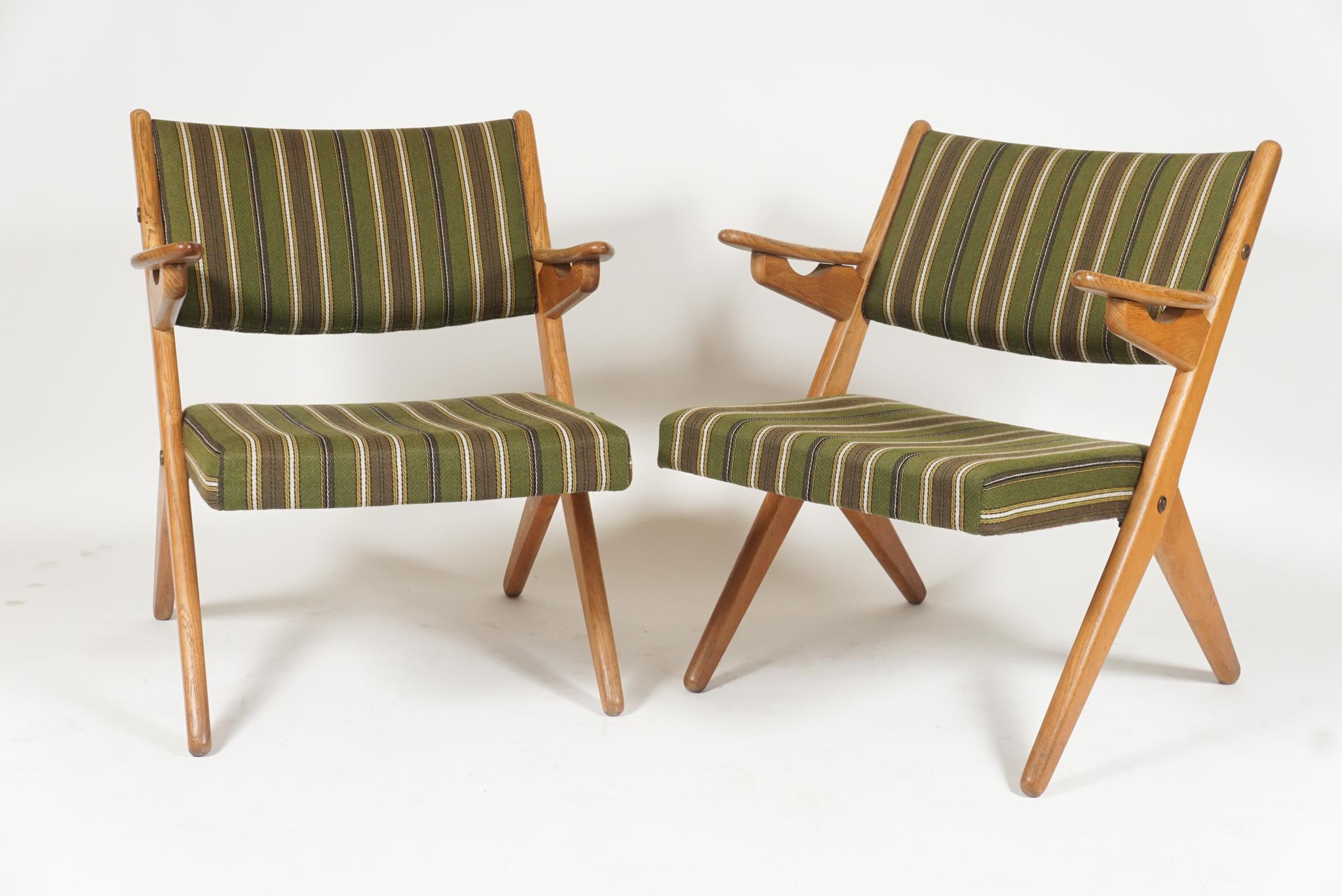 Sleek pair of Scandinavian easy lounge chairs reminiscent of Folke Ohlsson scissor chairs and Hans Wegner sawbuck chairs. Oak framed with original cushions and fabric. Great midcentury lines in a sleek pair of comfortable chairs.