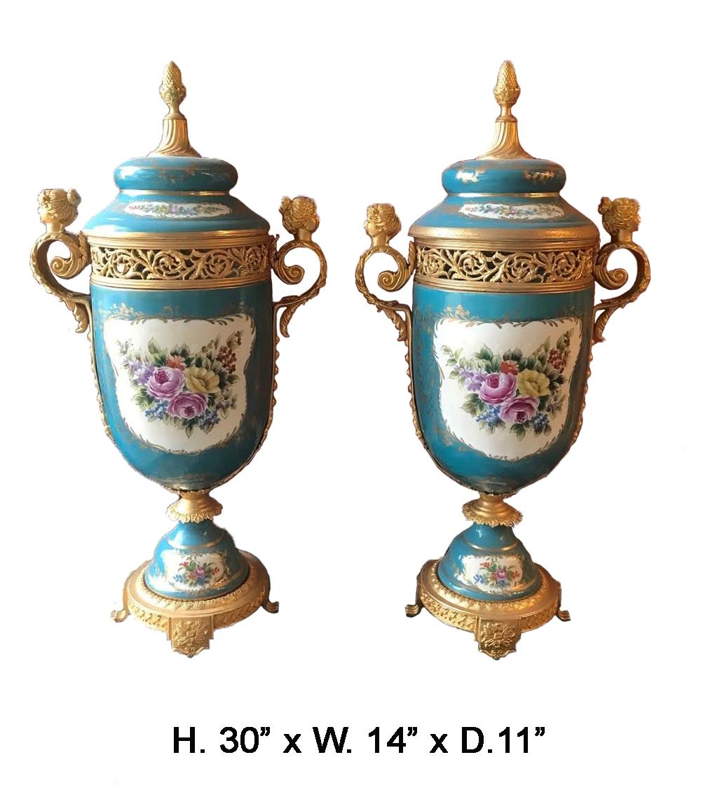 Beautiful French ormolu mounted Sevres style porcelain covered urns. 
The light blue porcelain is hand painted with a floral motif on both sides, the ormolu is on the finial and handles. 
The urns are resting on bronze bases.
Measures: H. 30