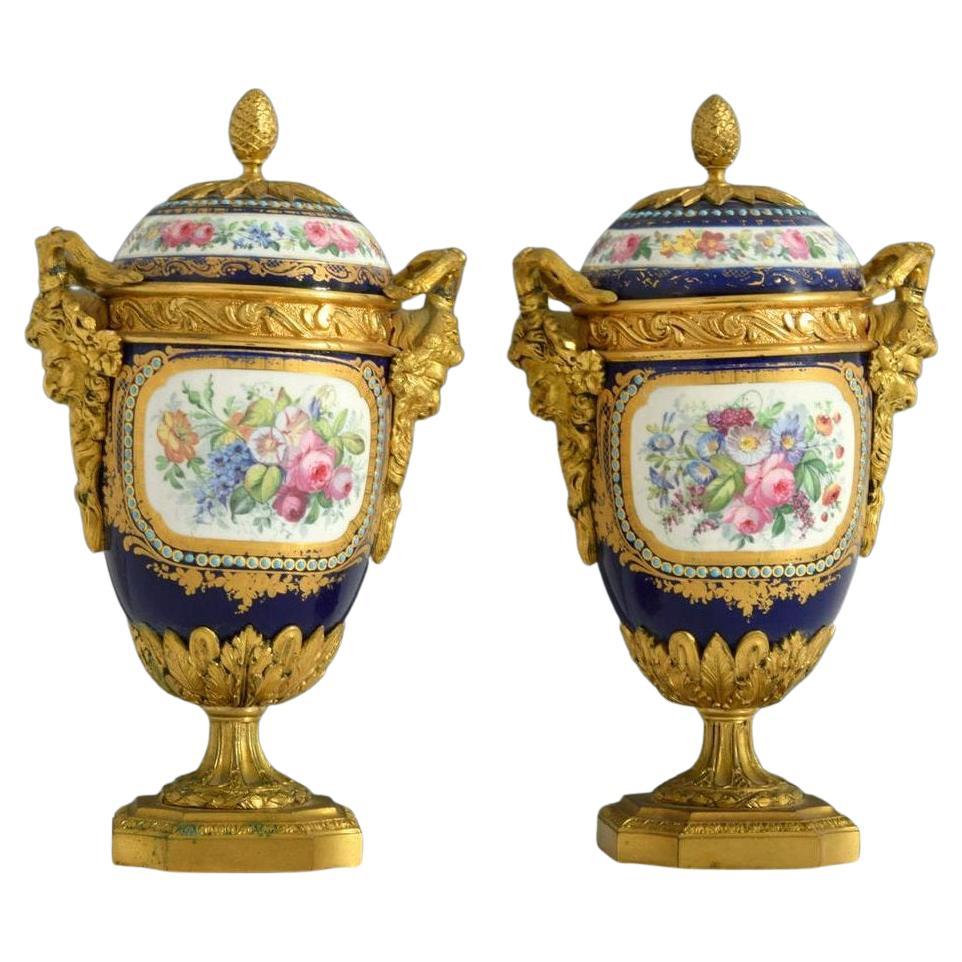Pair Sevres style Ormolu bronze mounted porcelain urns with covers. With hand-painted reserves depicting cherubs at play and floral bouquets, with jeweled decorations and neoclassical gilt bronze mounts including satyr handles and acanthus leaf