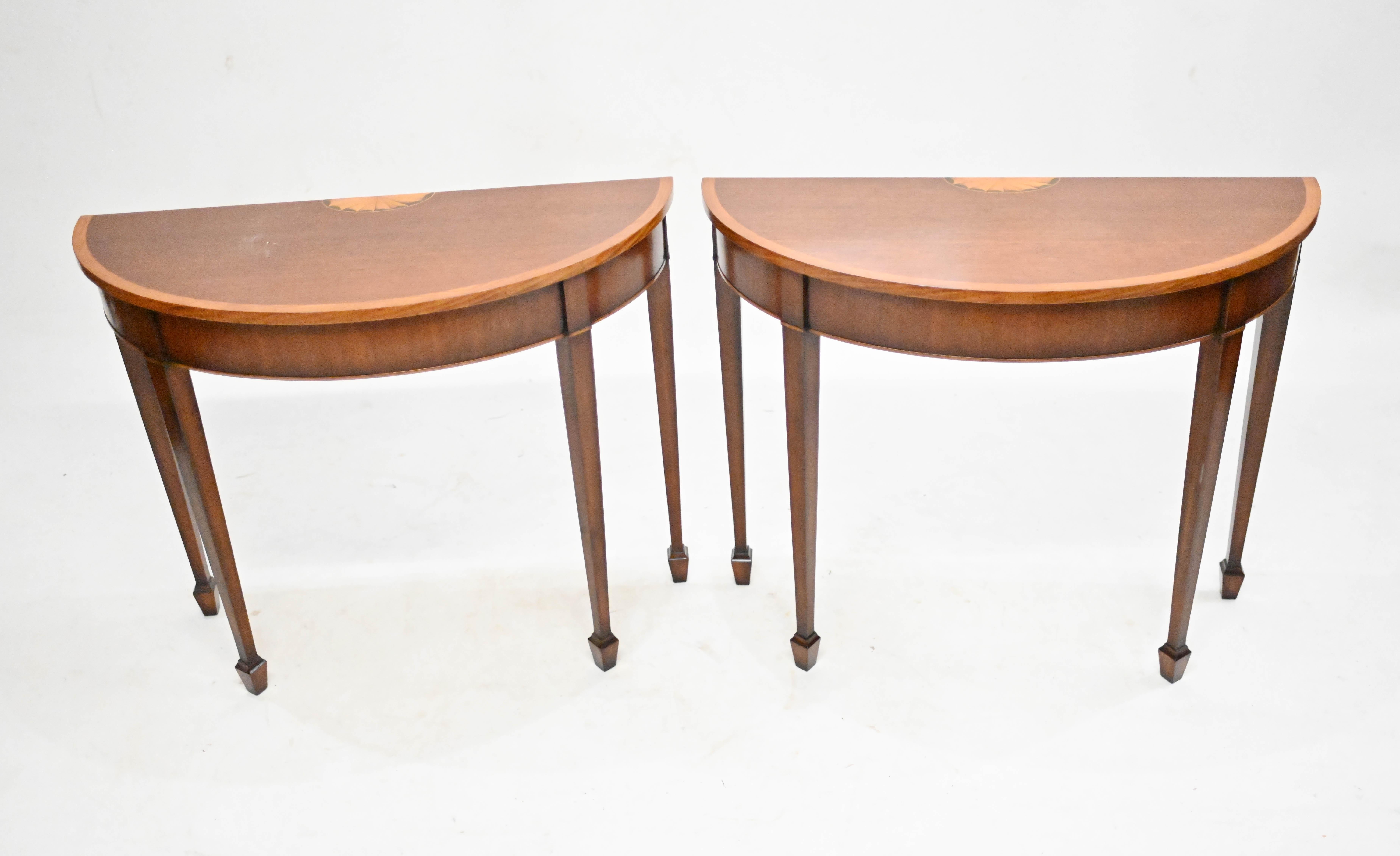 Pair of mahogany demi lune console tables in the Sheraton manner
Such an elegant and refined design with the tapered legs
Classic piece of furniture great for any interior
Features satinwood inlay, cross banding and a shell motif
Offered in great