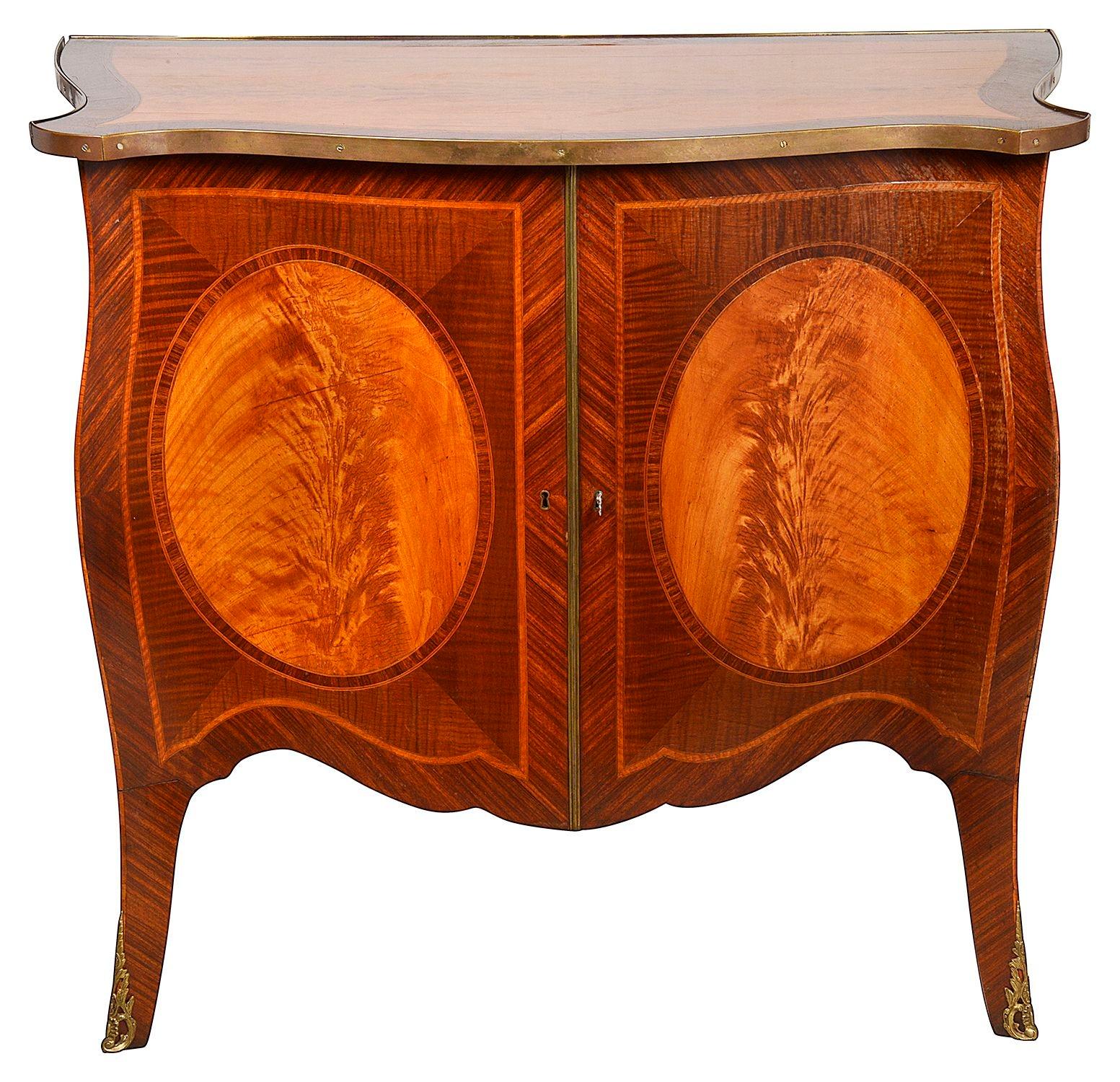 A good quality pair of Mahogany and Satinwood inlaid serpentine fronted Sheraton revival commodes, each with wonderful crossbanded tops, oval Satinwood inlay to the sides and doors, these open to reveal shelves within, raised on elegant out swept