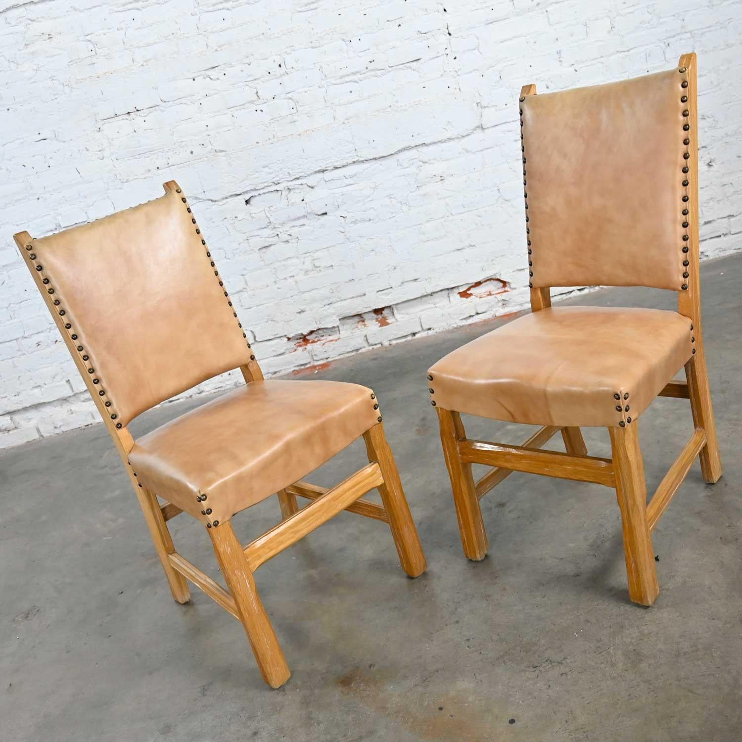 Wonderful pair of side chairs reupholstered in beige vinyl or faux leather with antiqued brass nail head trim details attributed to Ranch Oak by A. Brandt Company. Beautiful condition, keeping in mind that these are vintage and not new so will have