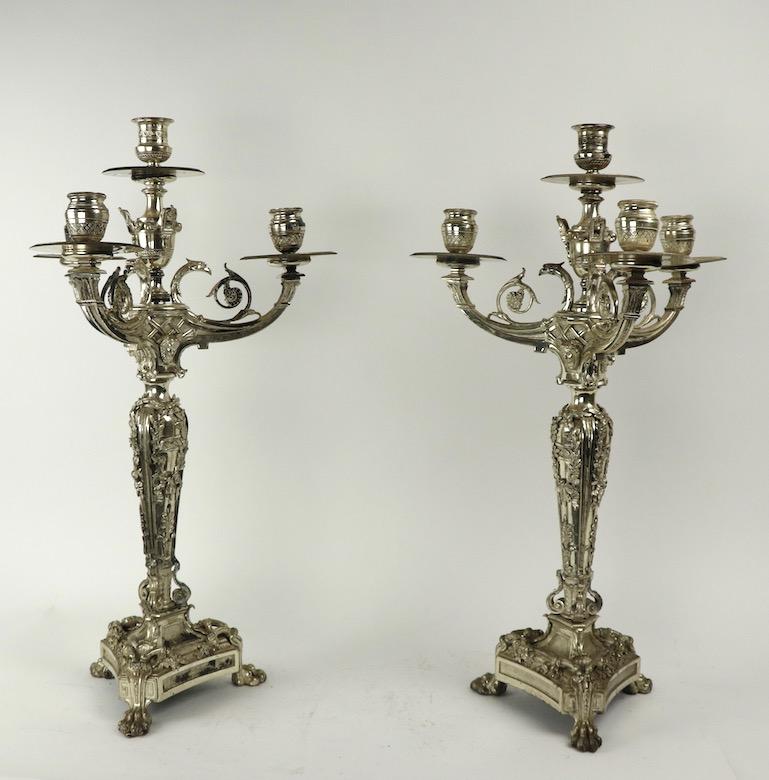 Pair of ornate silverplate candelabra, each having 4 candle cups, in original silver finish, finish shows some wear, normal and consistent with age. One candlestick is missing a small decorative element, see images.