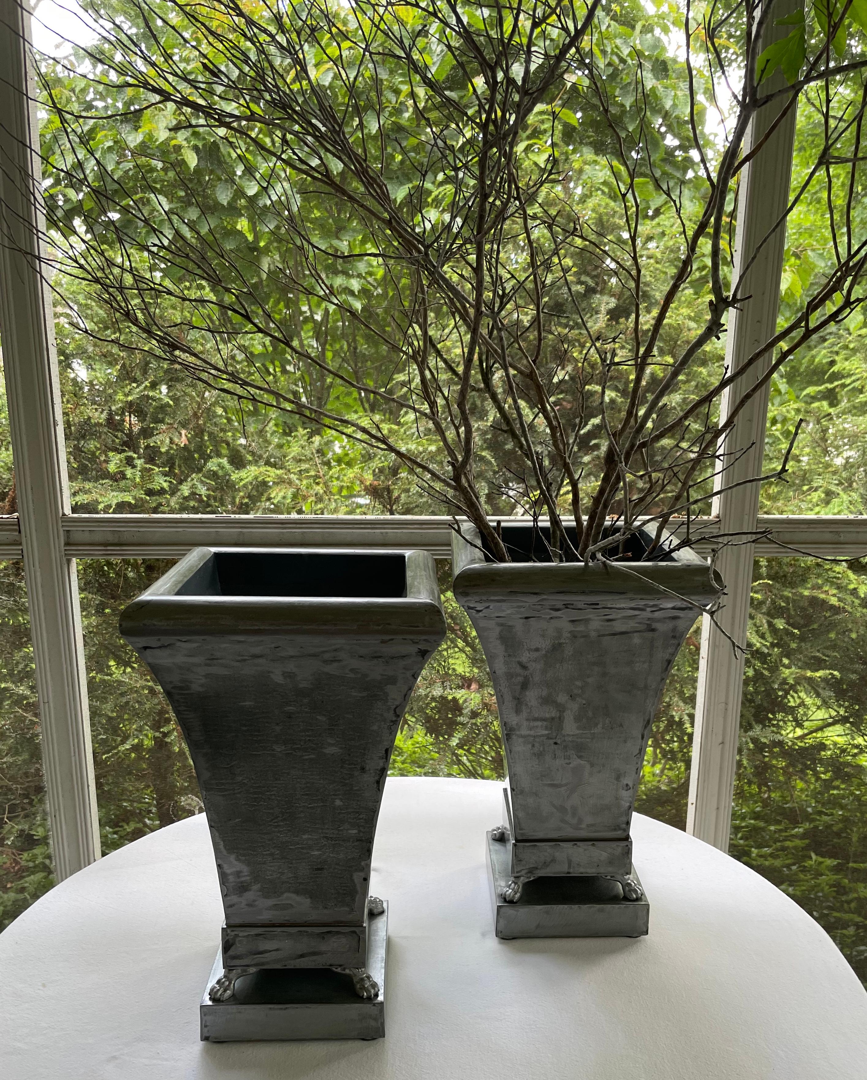 Pair silvered cachepot planters in neoclassical style. Pair large planters in waxed silver metal of tapered square form resting on lion paw feet on square plinths. American industrial style good in both modern and traditional setting. United States,