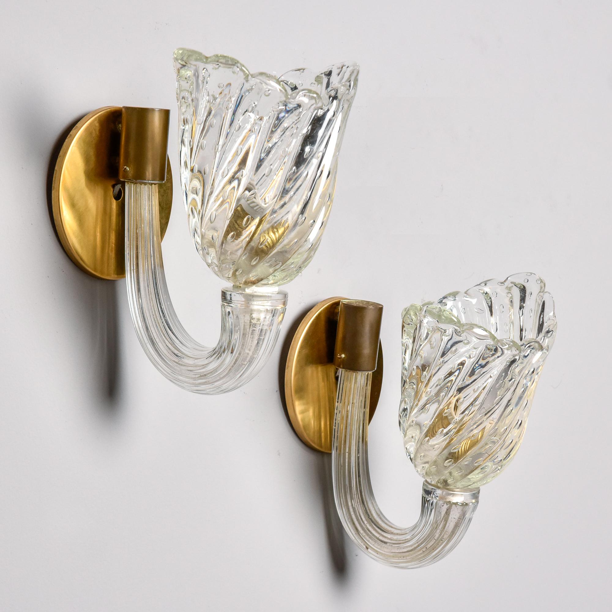 Found in Italy and attributed to Venini, these Murano glass sconces date from the 1950s. Each sconce has a round brass back plate, a single, thick ridged clear glass arm and ridged, tulip-form globe/shade with scalloped rim and bullicante