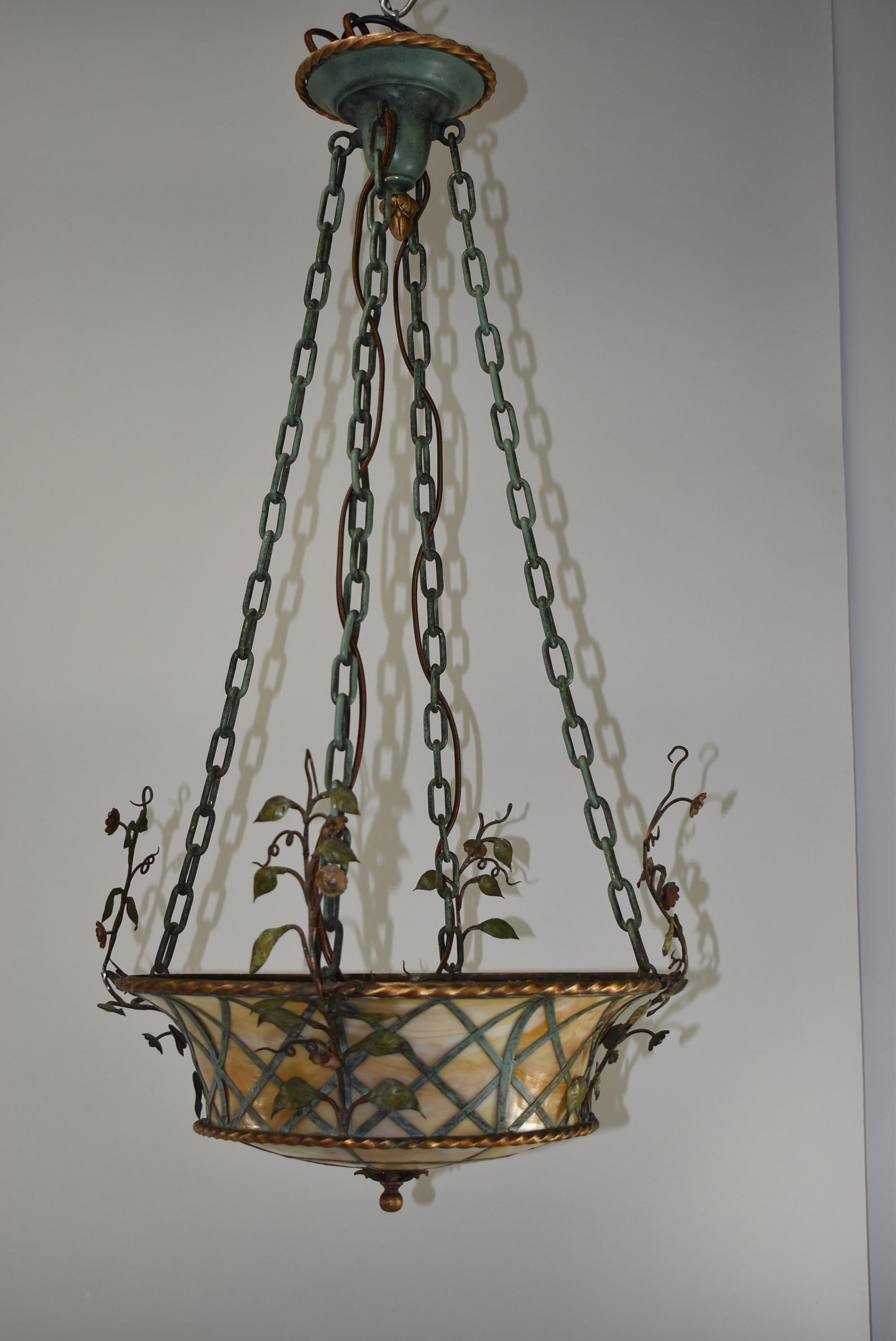 Pair of slag glass 1920s basket form brass and iron chandeliers with hand painted leaf and vine details. Amber bent glass panels. Spiral brass trim rings. Original ceiling caps.
