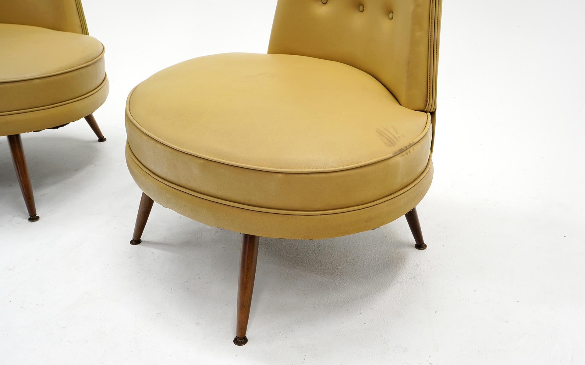 Striking pair of armless slipper chairs in the original mustard yellow vinyl. Walnut legs with brass caps. These can be used as is but we have them priced expecting the new owner may want to reupholster them. The wide seat, high back and splayed