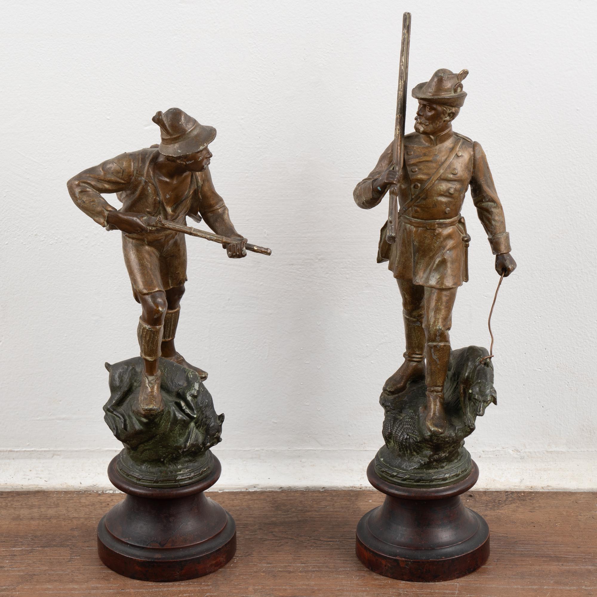 Pair of sculptures of two hunters in the field. The gentleman hunter has rifle and dog on leash while his country assistant has rifle and what appears to be a deer at his feet.
Bronze finish shows age related wear including tarnish, small nicks,