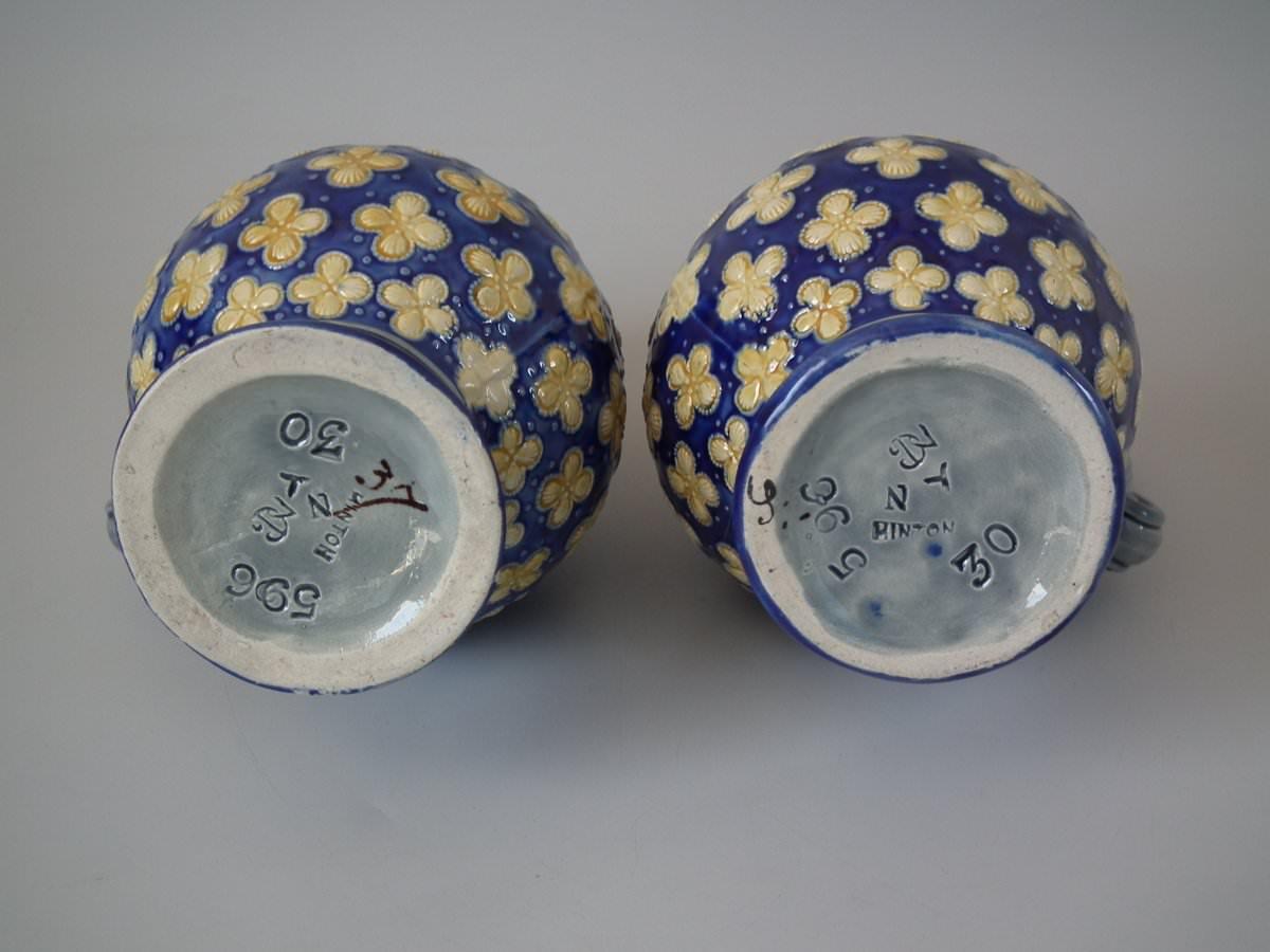 Pair of Minton majolica jug or pitchers which feature shells arranged in quatrefoil shapes. Colouration: cobalt blue, ochre, grey, are predominant. Bears a pattern number, '596'. Marks include a factory specific date cipher for the year 1871.