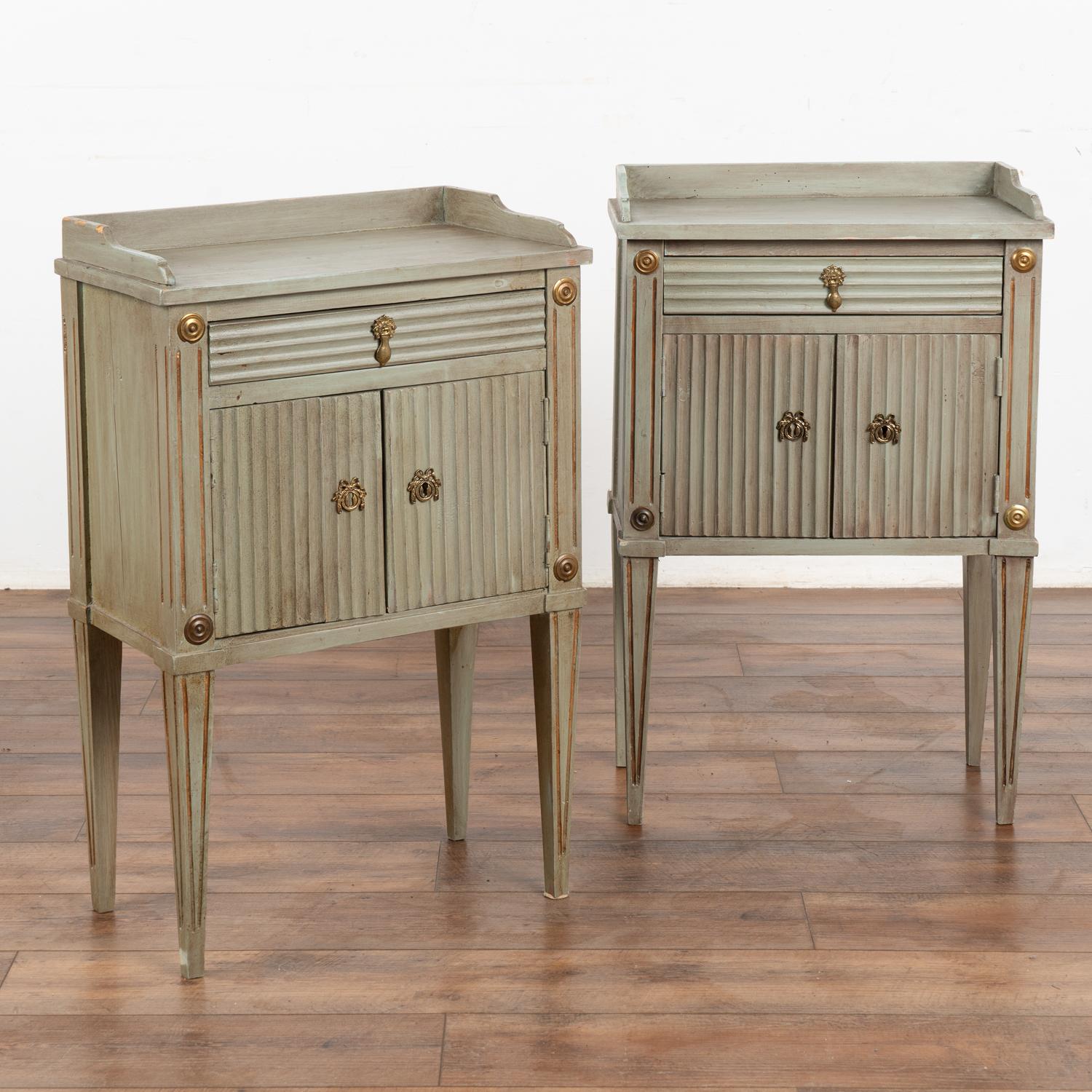 This pair of small Swedish country cabinets stand on elongated tapered legs and may serve well as a nightstands or side tables.
While the painted finish is old, it is not original to the set. Shades of pale teal, gray and accents of gold are seen by
