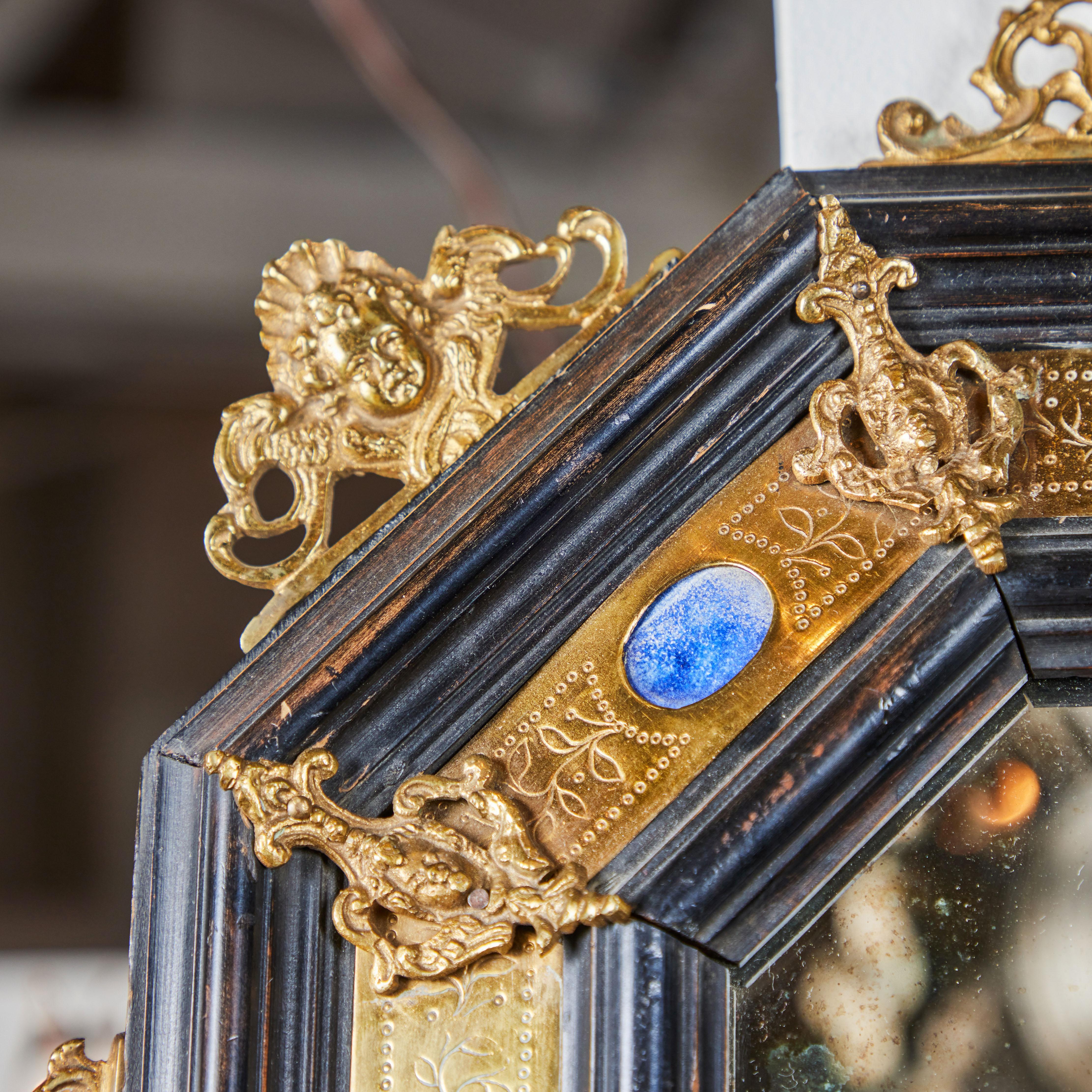 Paire de miroirs octogonaux de style Renaissance, en bois ébonisé, laiton gravé et bronze doré, sertis de pierres semi-précieuses plaquées. Les visages des chérubins sont ornés de détails en bronze doré. Le miroir d'origine est marbré en fonction de