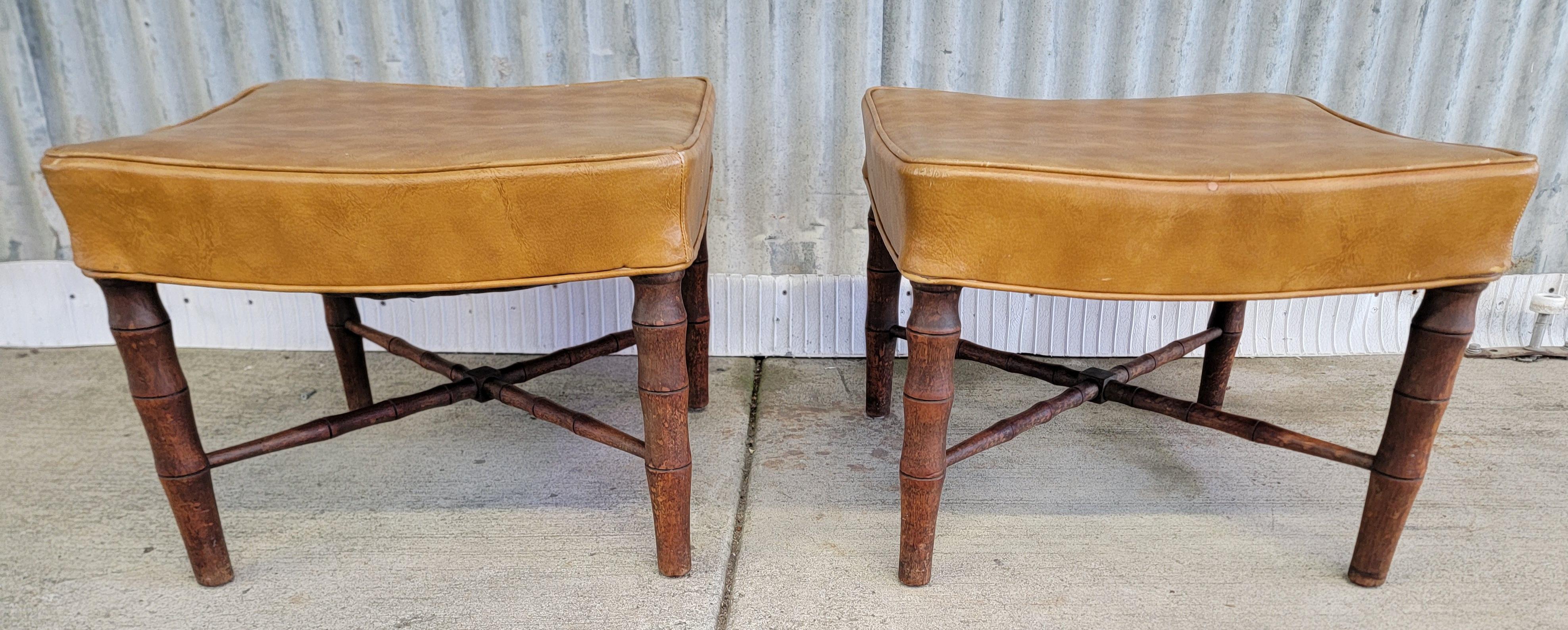 A pair of turned mahogany footstools or ottomans with a faux bamboo detail. Circa. 1950's. Older re-upholstery with a shop tag dated 1970. Presentable as they are, but there is light wear to vinyl upholstery and the solid mahogany frames have