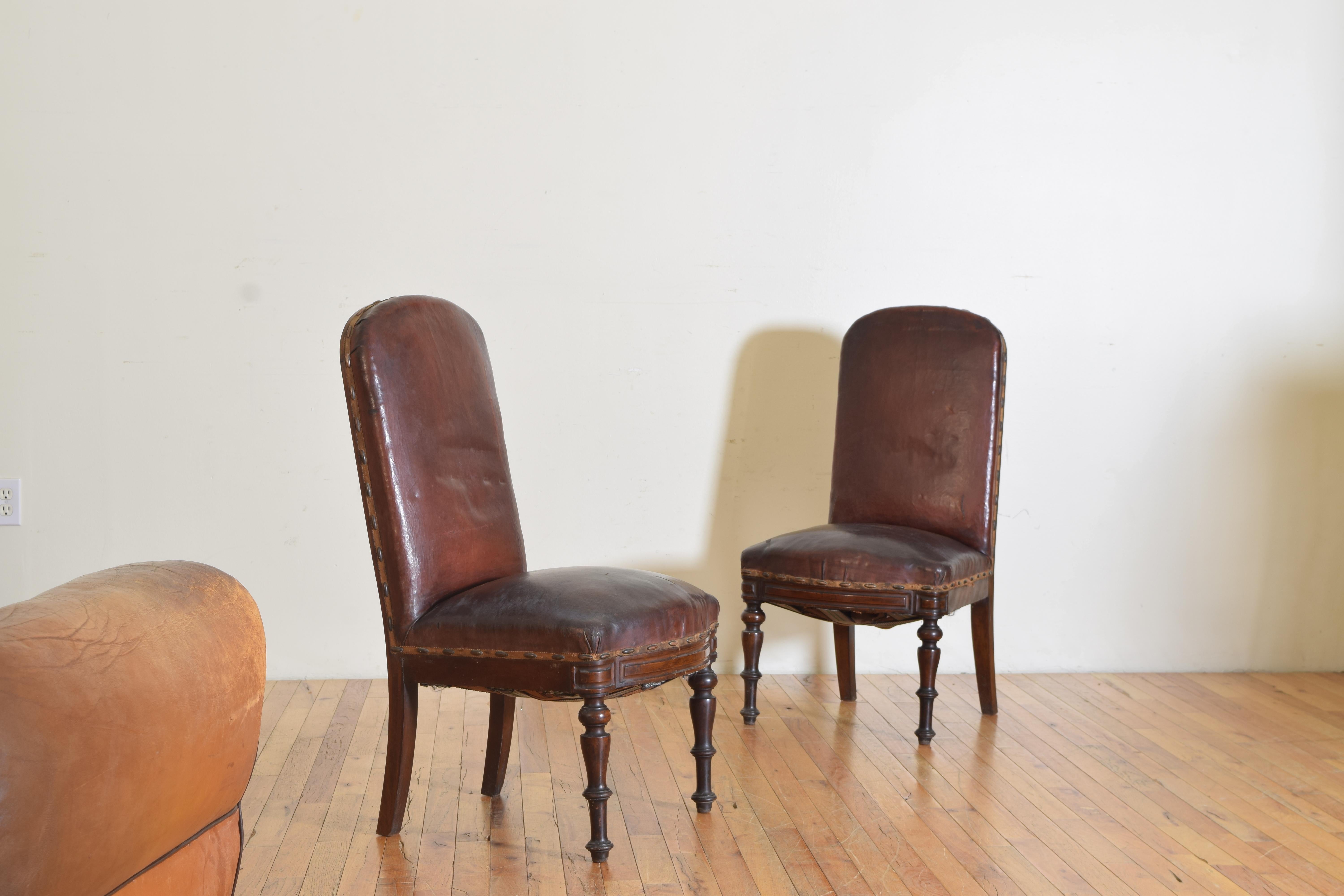 Each chair having a rounded back rest, seats and back in original leather trimmed in large brass nailheads, raised on round tapering legs