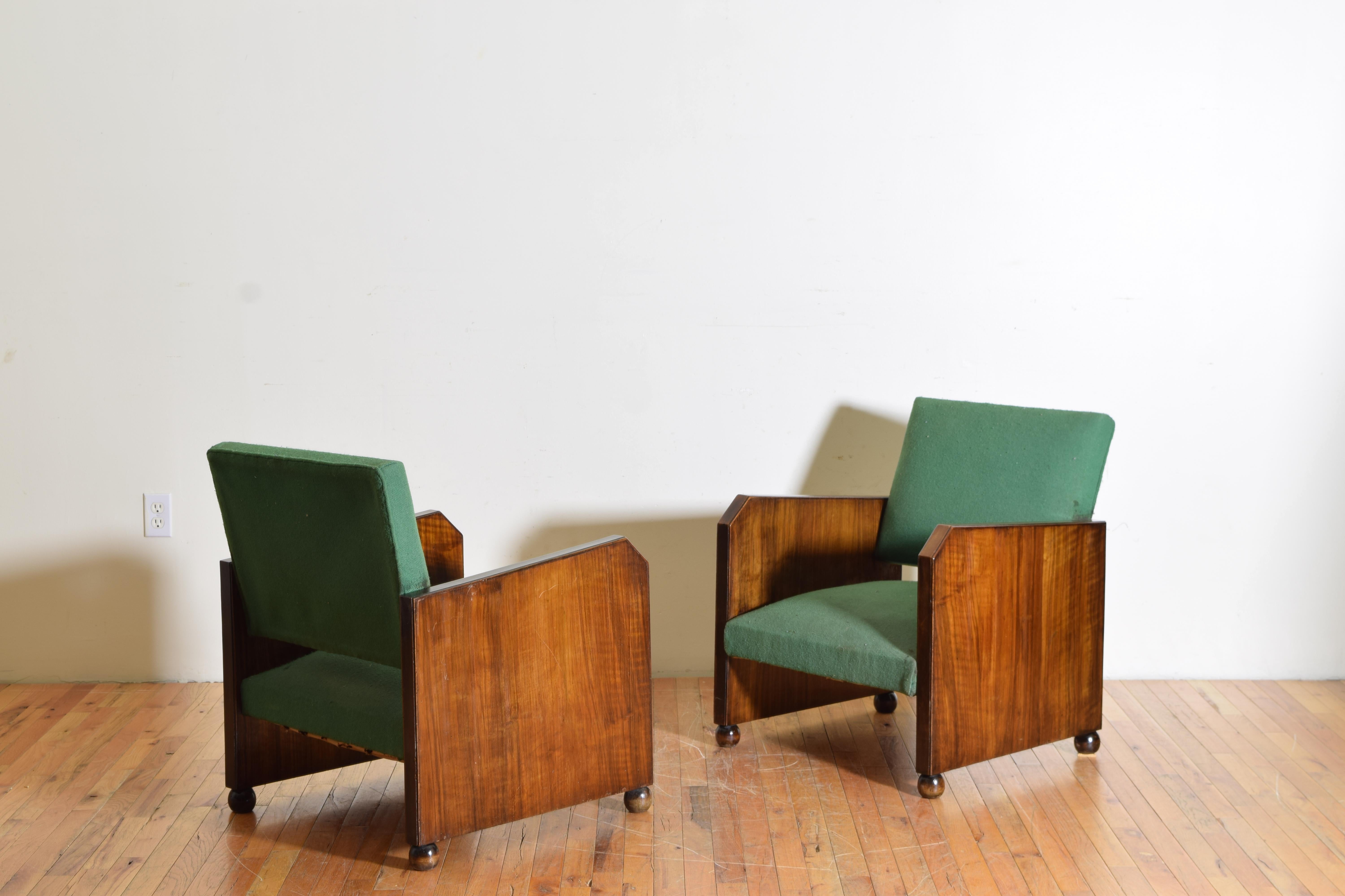 Having shaped sides of walnut and raised on small bun feet this pair of club chairs, retaining viintage upholstery.