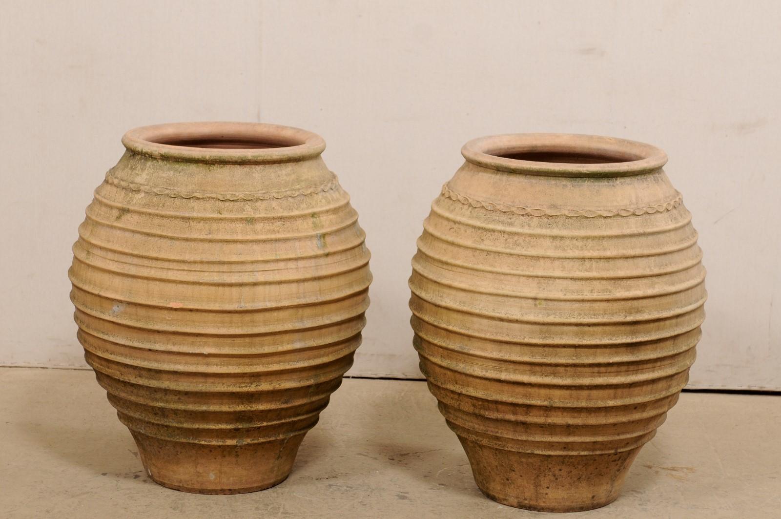 A Spanish pair of terracotta pots from the early 20th century. This pair of antique terracotta bulb-shaped vessels from Spain each have with a thick and rounded lips at top opening, an ornate decorative trim at top perimeter of body, followed by