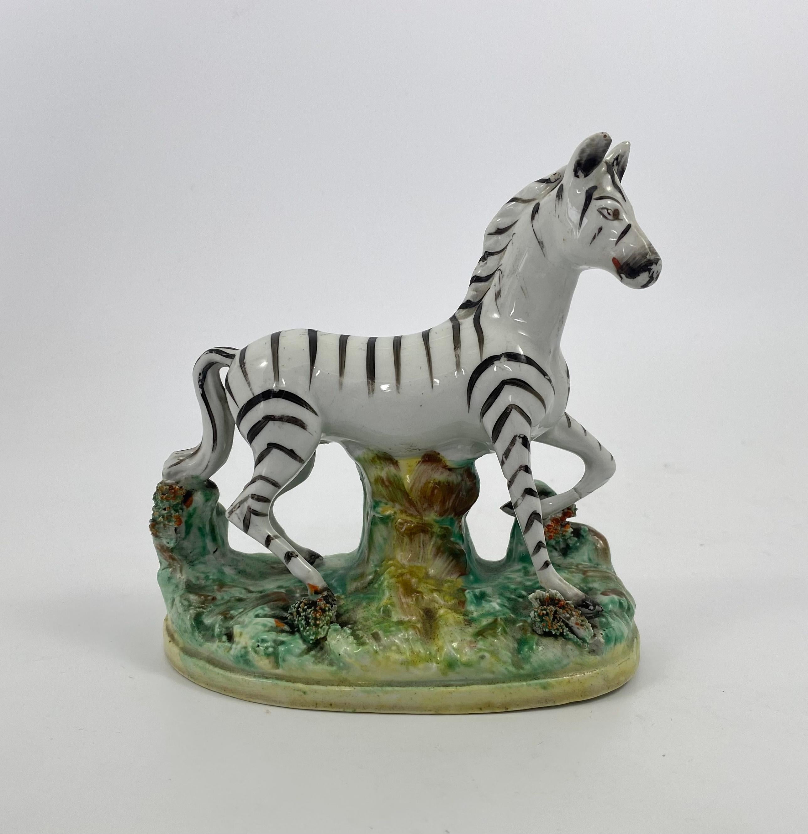 Pair Staffordshire pottery Zebra, Thomas Parr factory, c. 1860. Finely modelled, supported by tree trunks, upon oval grassy mound bases, painted in underglaze enamels, and encrusted with clumps of grass. Their stripes in black overglaze