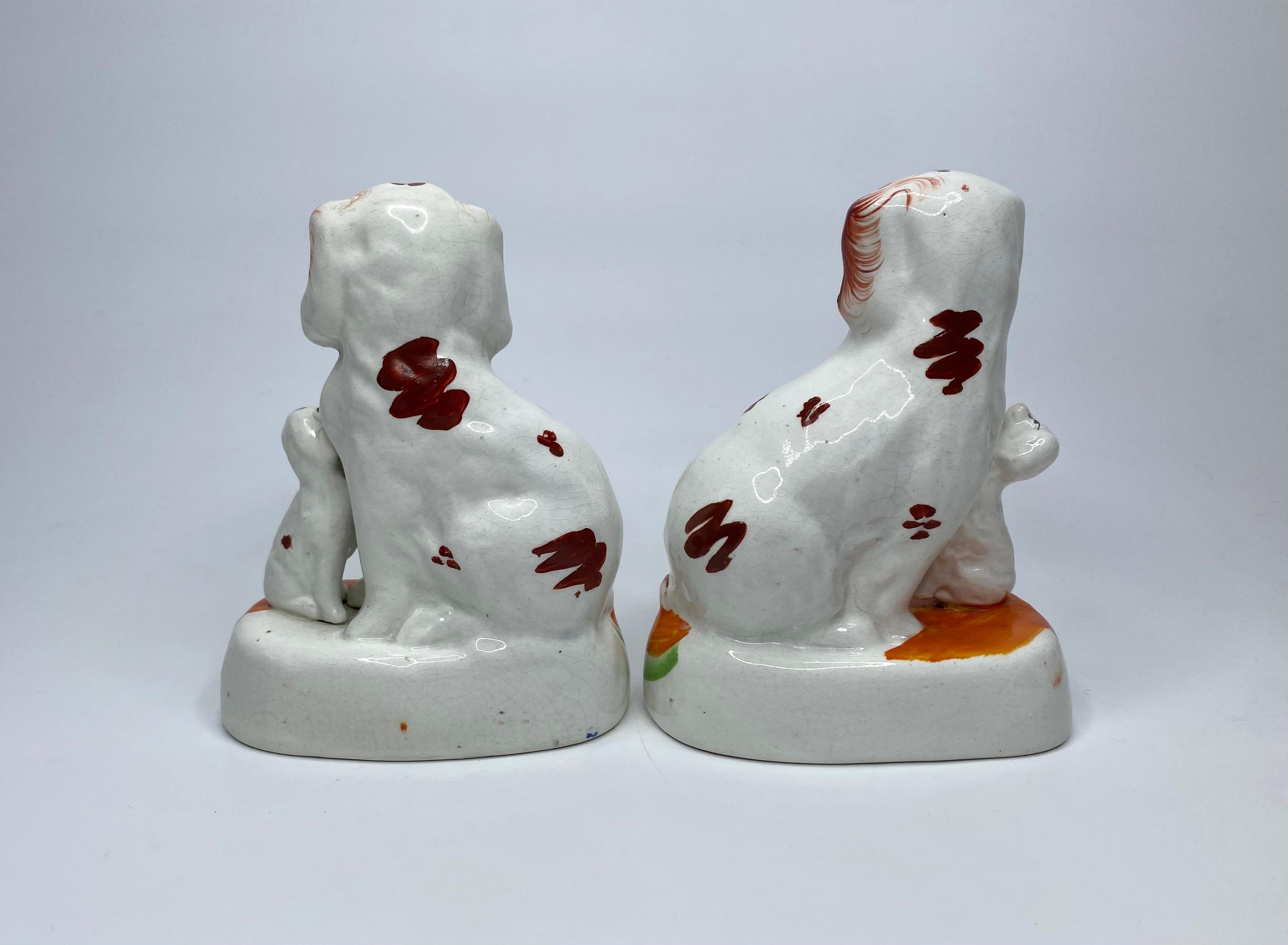 Pair of Staffordshire pottery Spaniels with puppies, c. 1850. Charmingly modelled, as seated Spaniels, with their puppies, painted with liver red spots, feathered at the edges. Both groups, set upon orange coloured cushion bases, with gilt and blue