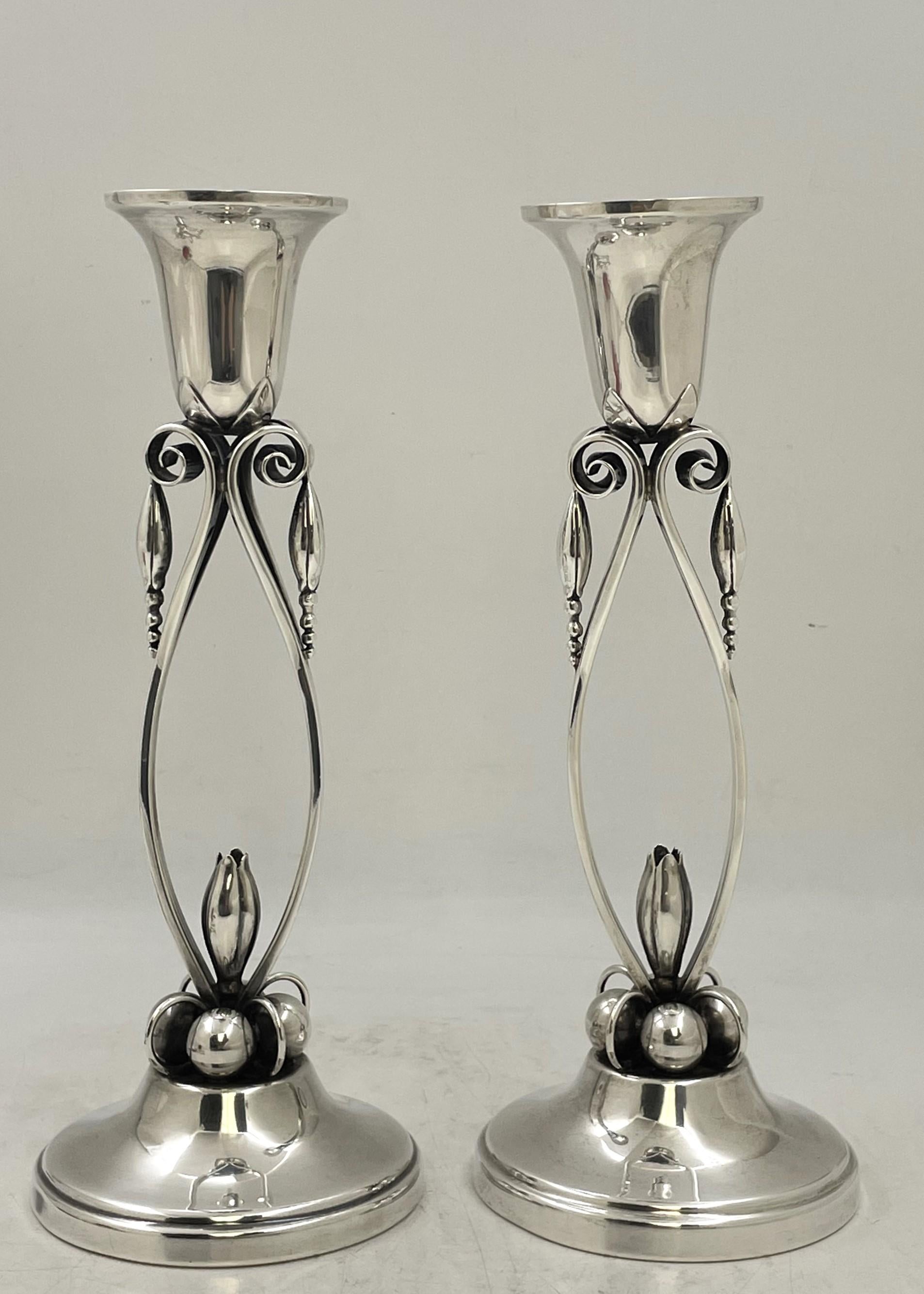 Coppia di candelieri in argento, in uno stile simile a quello del grande produttore danese Georg Jensen e in stile Mid-Century Modern, ornati da motivi geometrici e floreali stilizzati. Misurano 10 1/2'' di altezza per 2 1/2'' di diametro nella