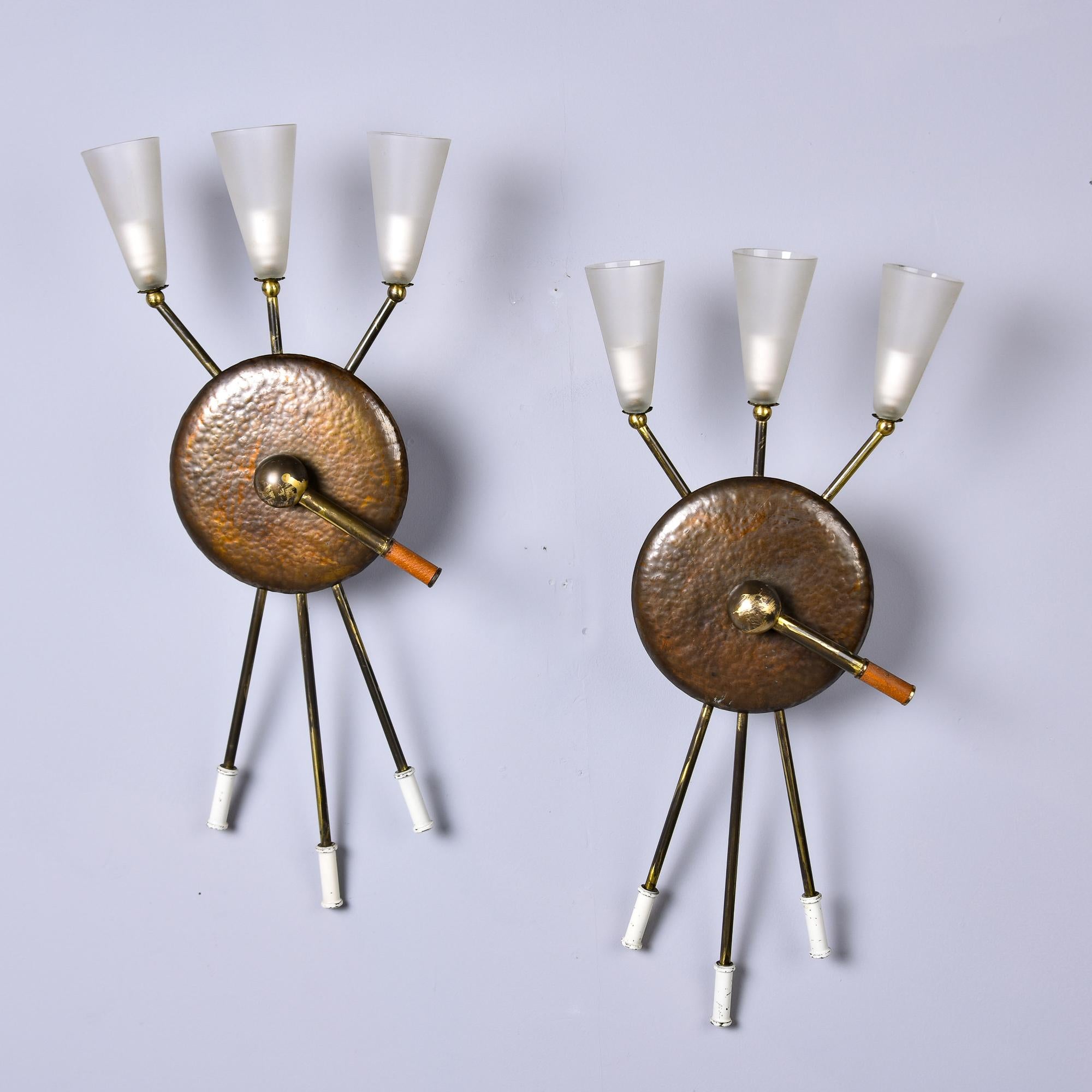 Found in Italy and attributed to Stilnovo, this pair of three light brutalist style sconces date from the late 1960s. Sconces feature a hammered copper center with slender brass stems supporting three frosted glass globes with candelabra sockets.