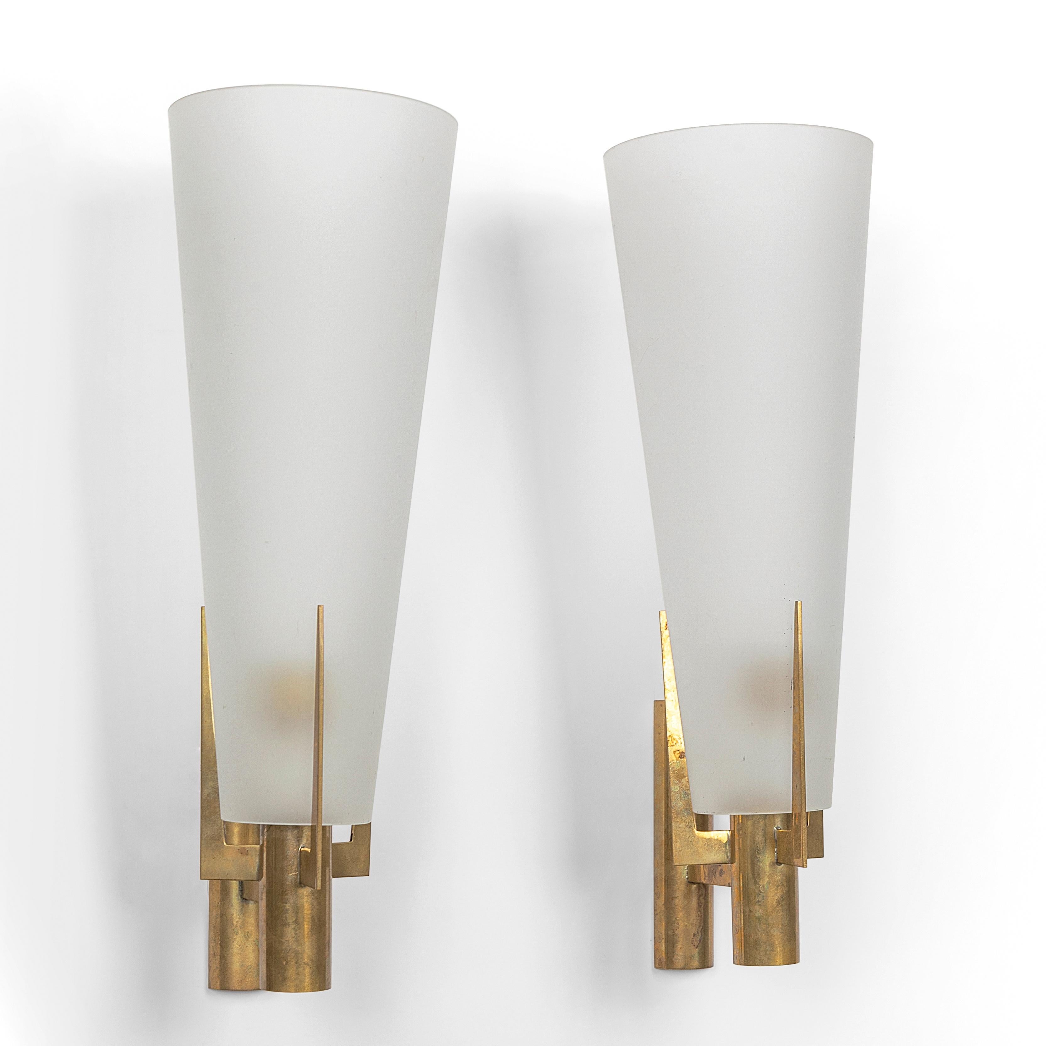 Elegant pair of original large scale wall sconces by Stilnovo, Model 2021/1 produced in Italy 1959-1960. Brass three pronged armature and tapered satin glass conical shades. 19.5 inches tall.
Each sconce has a single standard size Edison screw