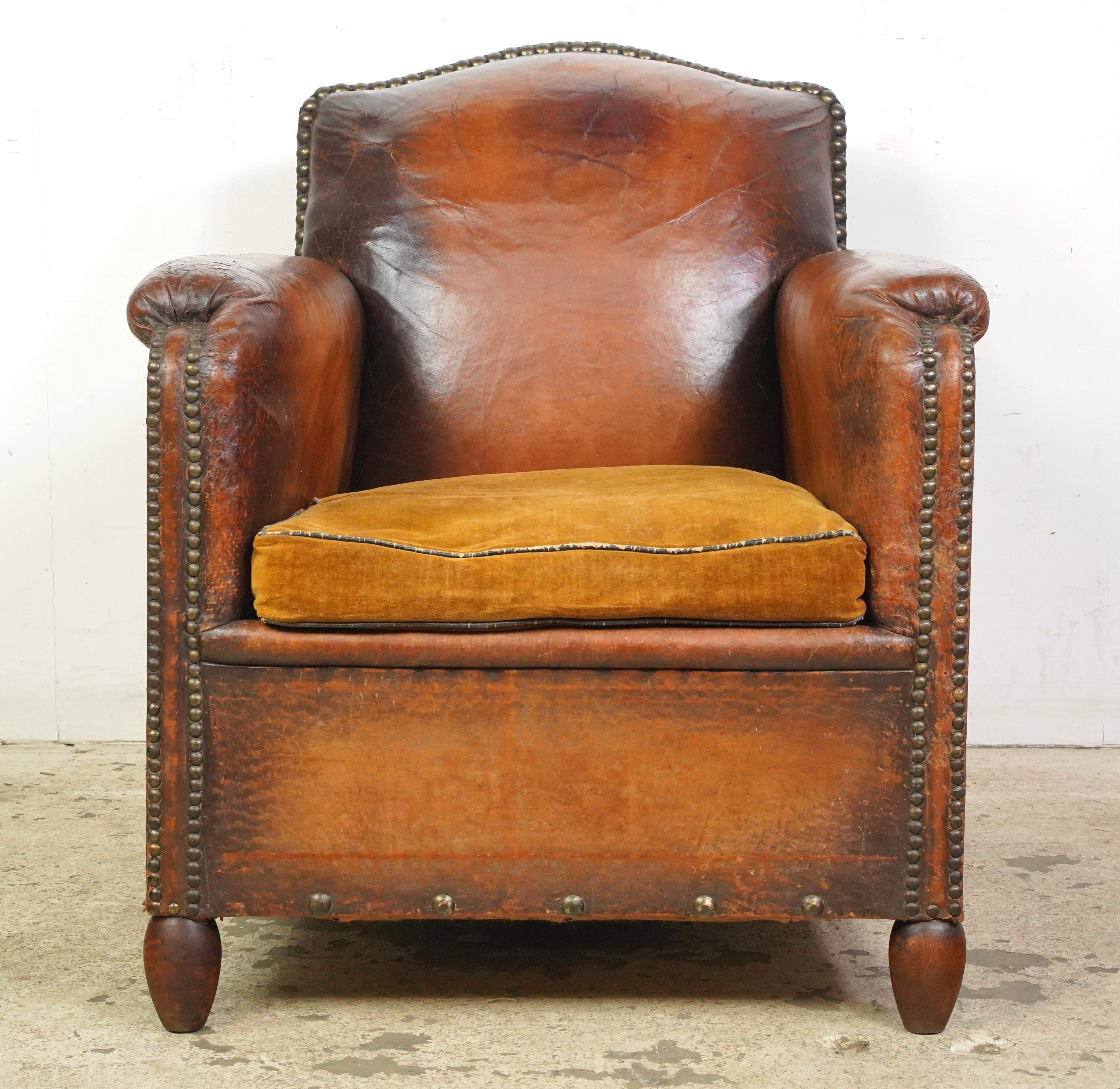 Paire de fauteuils club en cuir marron foncé fabriqués en France. Ils sont dotés d'un haut dossier incurvé, d'une assise rembourrée en peluche de couleur marron clair, de détails cloutés et de pieds en bois. Le cuir et les pieds présentent des