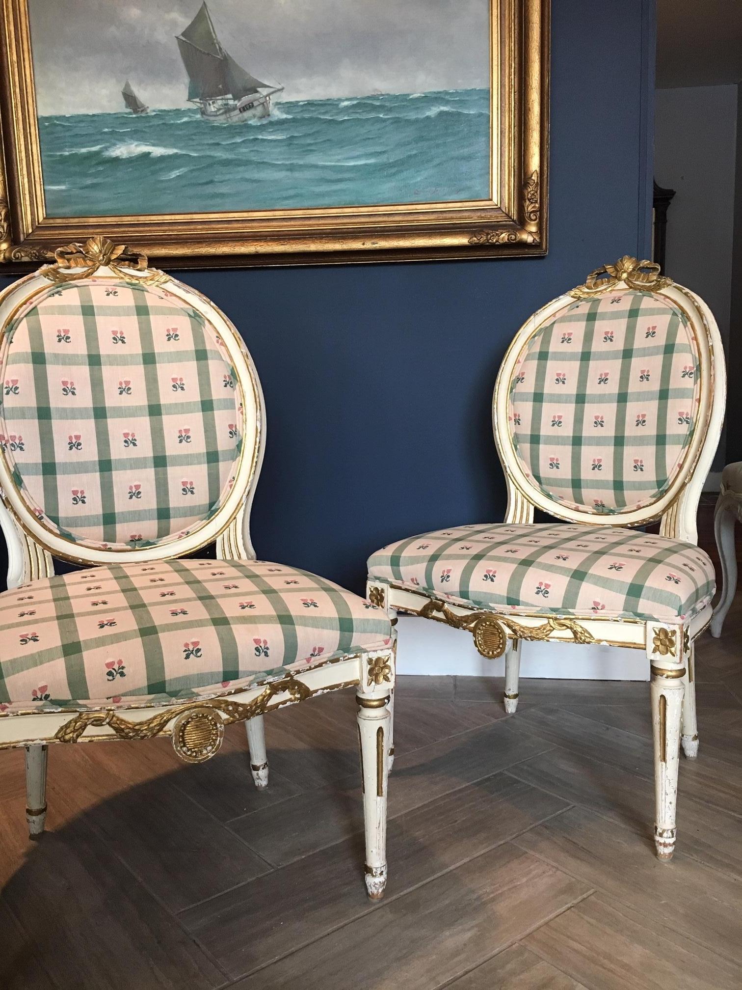 Gorgeous pair of Swedish side or salon chairs, painted and parcel gilt, in the Gustavian or Louis XVI style, 19th century. Crested by carved ribbons, with medallion motifs. Beautifully curved back.

Forms a set with pair of stools or tabourets,