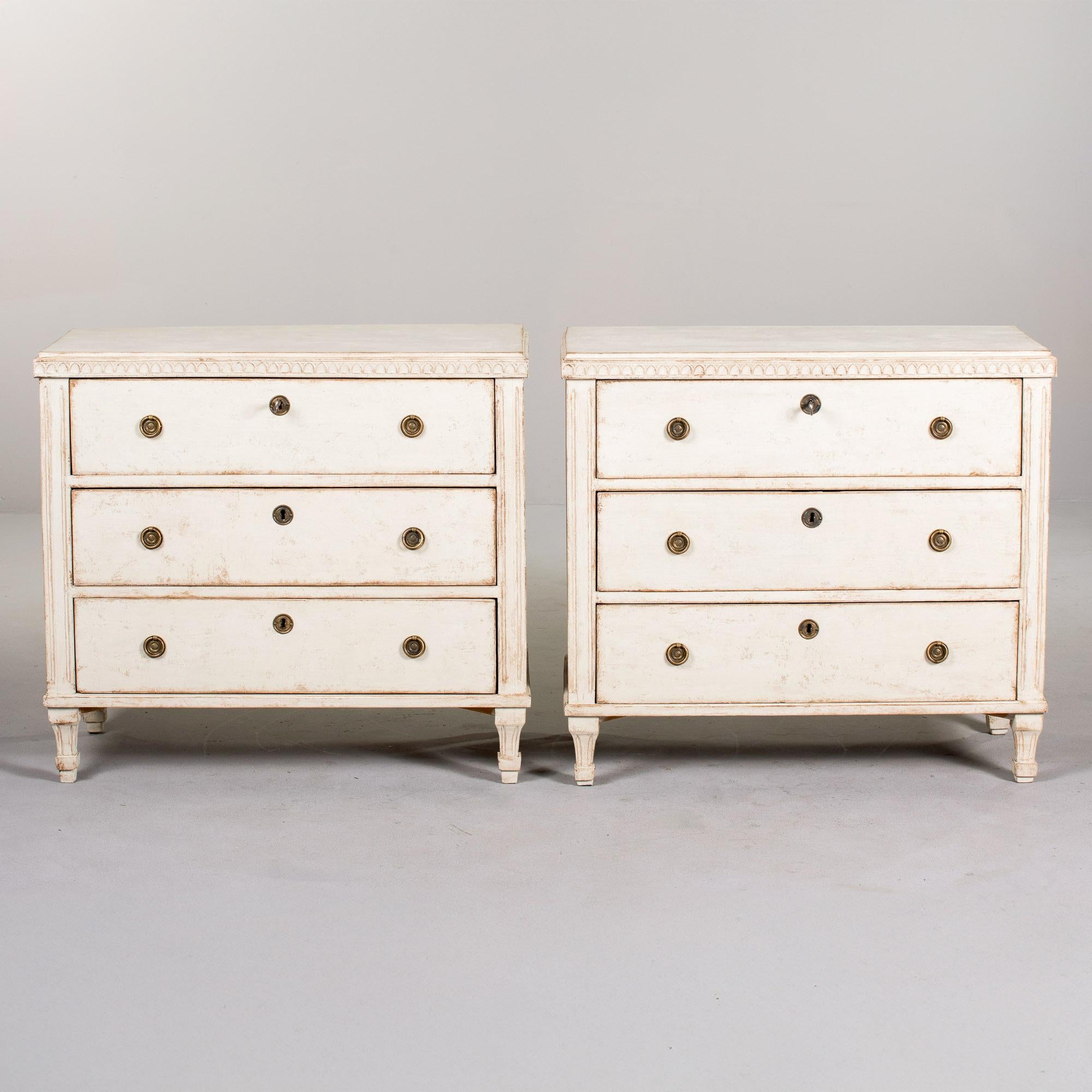 We estimate this pair of Swedish Gustavian painted chests to date from the 1860s. The three drawer chests have functional locks and each chest has a skeleton key. Brass pull-ring hardware and escutcheons. Antique white painted finish, dovetail