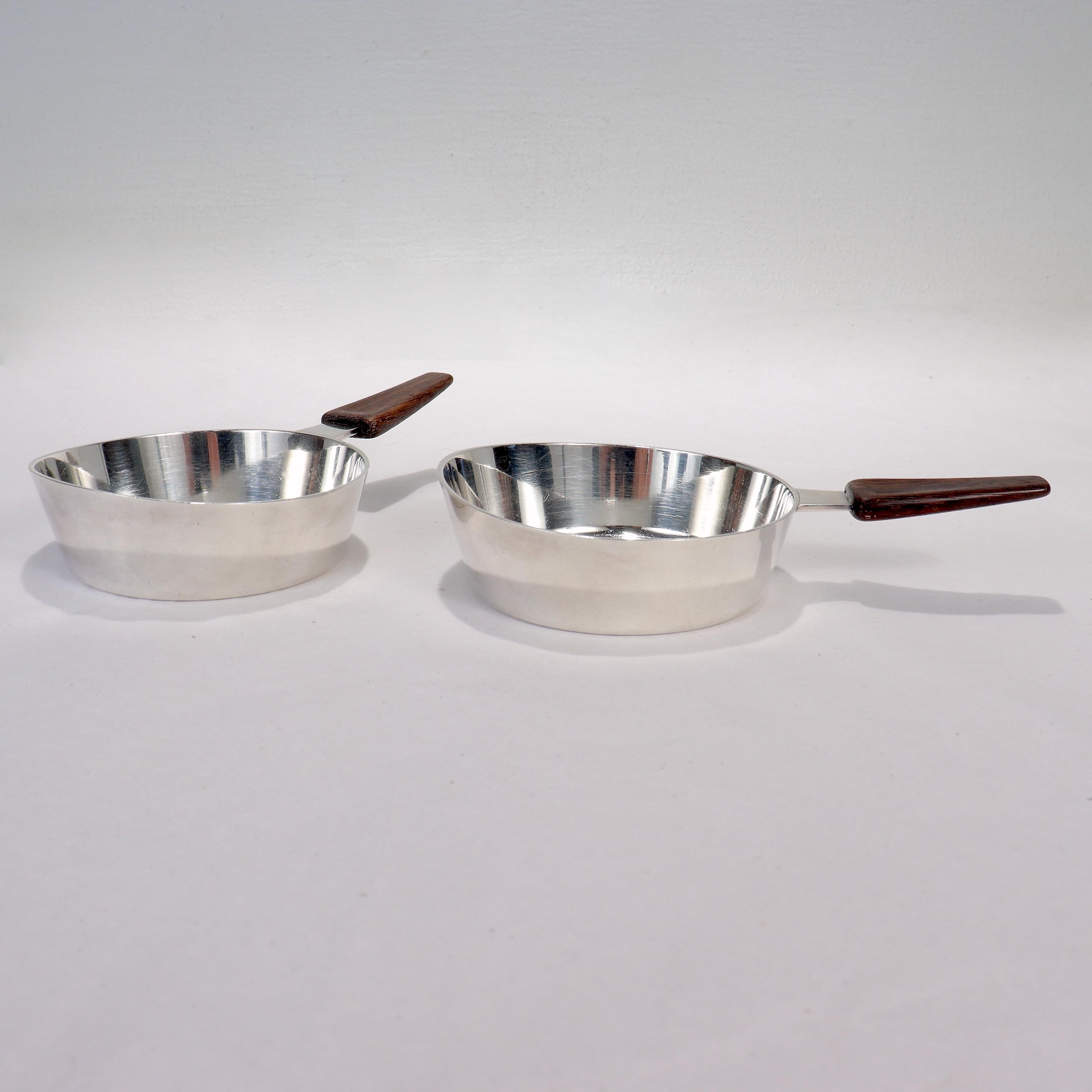 A fine pair of Mid-Century Modern sterling silver and wooden handled dishes.

Possibly designed as raclette dishes, the pieces resemble small pans. Perfect nowadays for as bowls for a Modernist cocktail tray or service.

The attached wooden handles