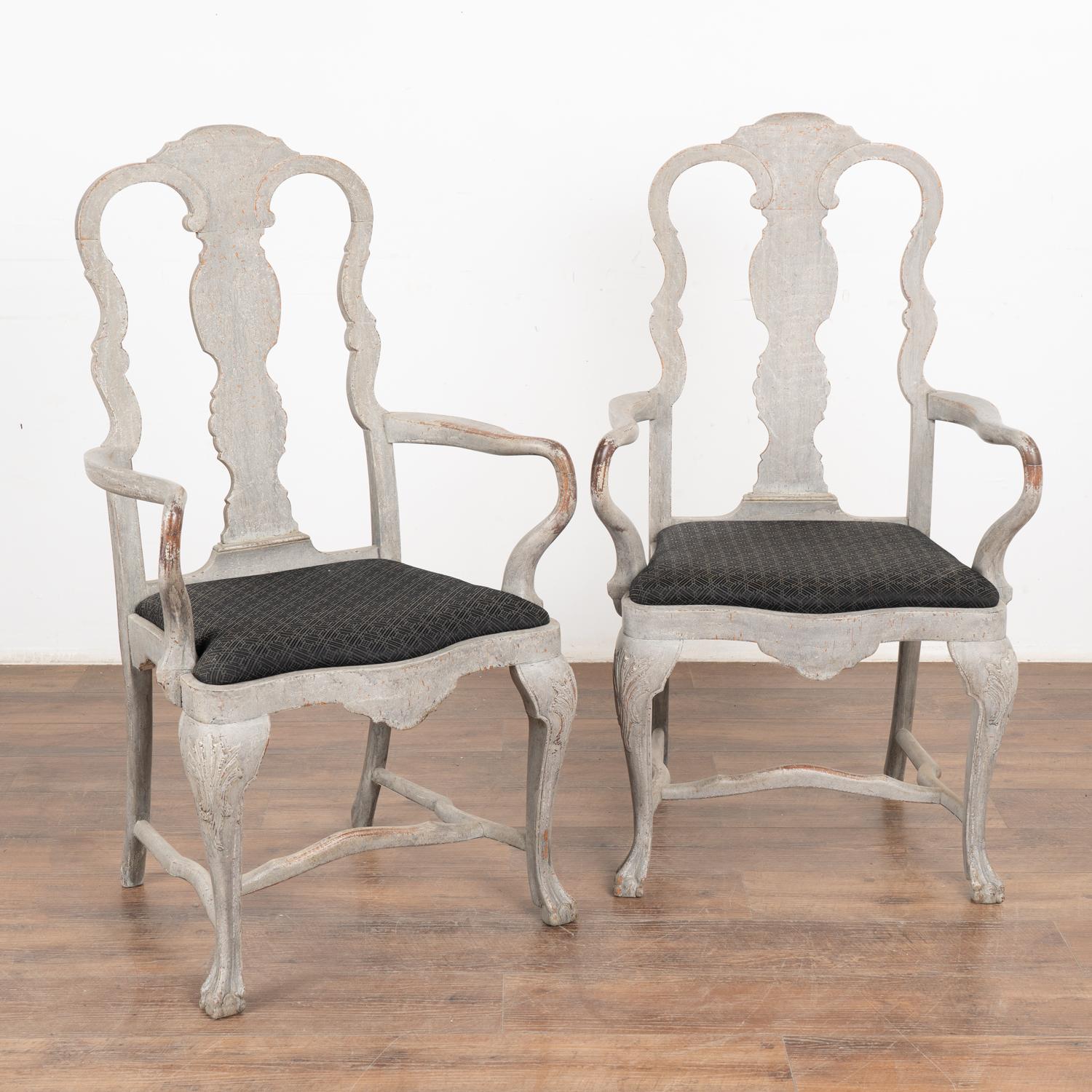 Filled with curves and graceful lines, this pair of Rococo style Swedish arm chairs have a soft gray painted finish.
Distress to the dove gray painted finish is seen throughout, in particular around the arm rests.
The upholstered seats pop out, so