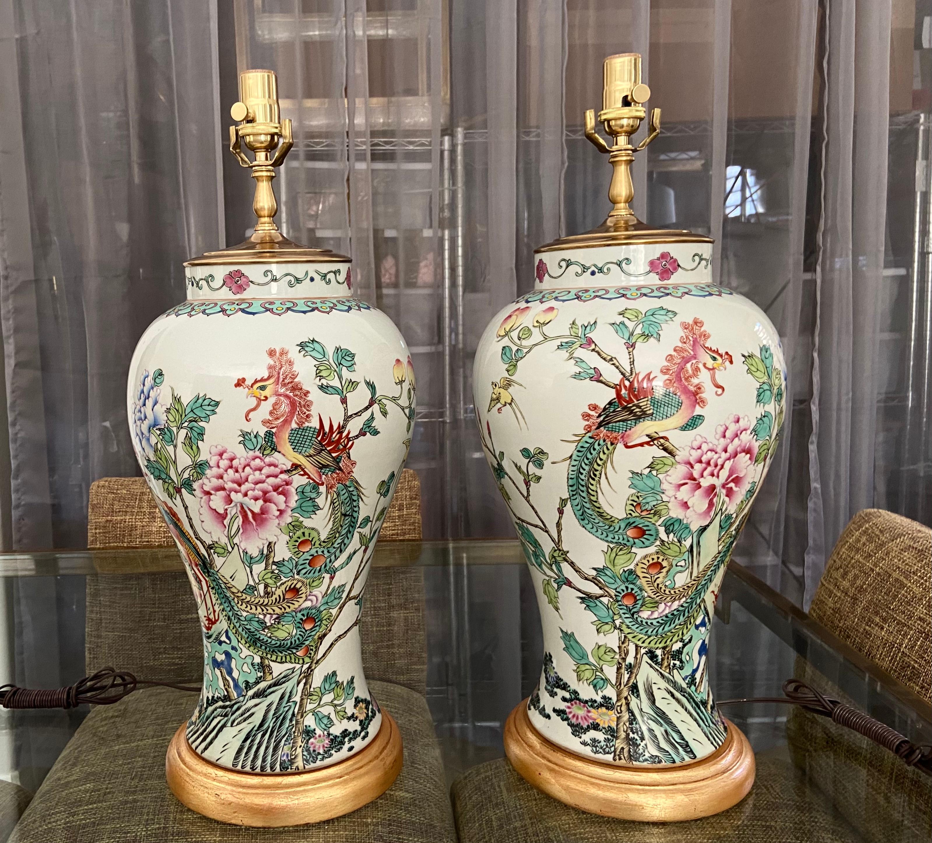Pair of Chinese import porcelain Famille Rose vases mounted as table lamps on giltwood turned bases. Beautifully crafted with colorful painted peacocks, and floral images, as well as birds and butterflies. Newly wired including new brass fittings