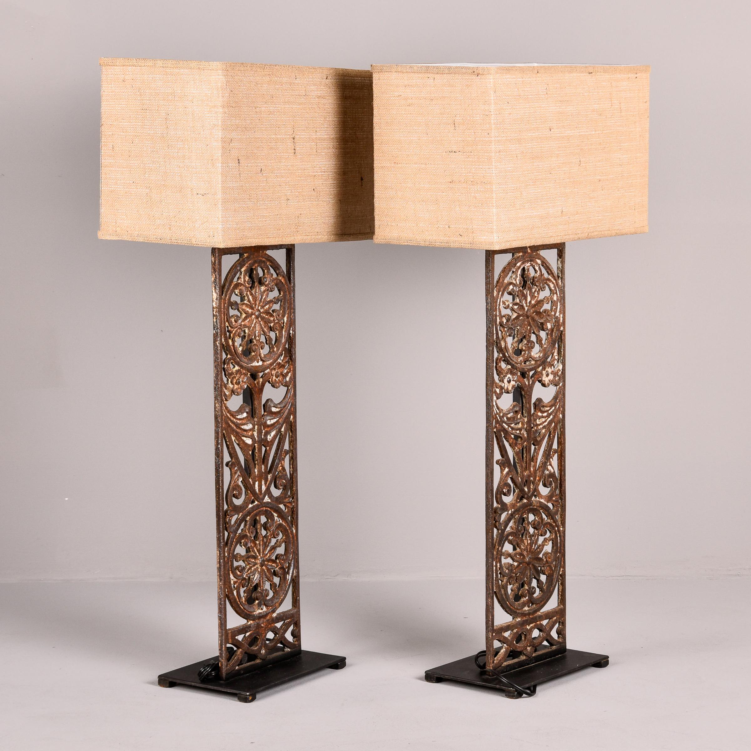 This pair of tall table lamps were custom made from 19th century Belgian decorative iron gate fragments. The tall, antique gate fragments are welded to new, black iron footed bases.  Each lamp has a brass harp and custom-made rectangular burlap