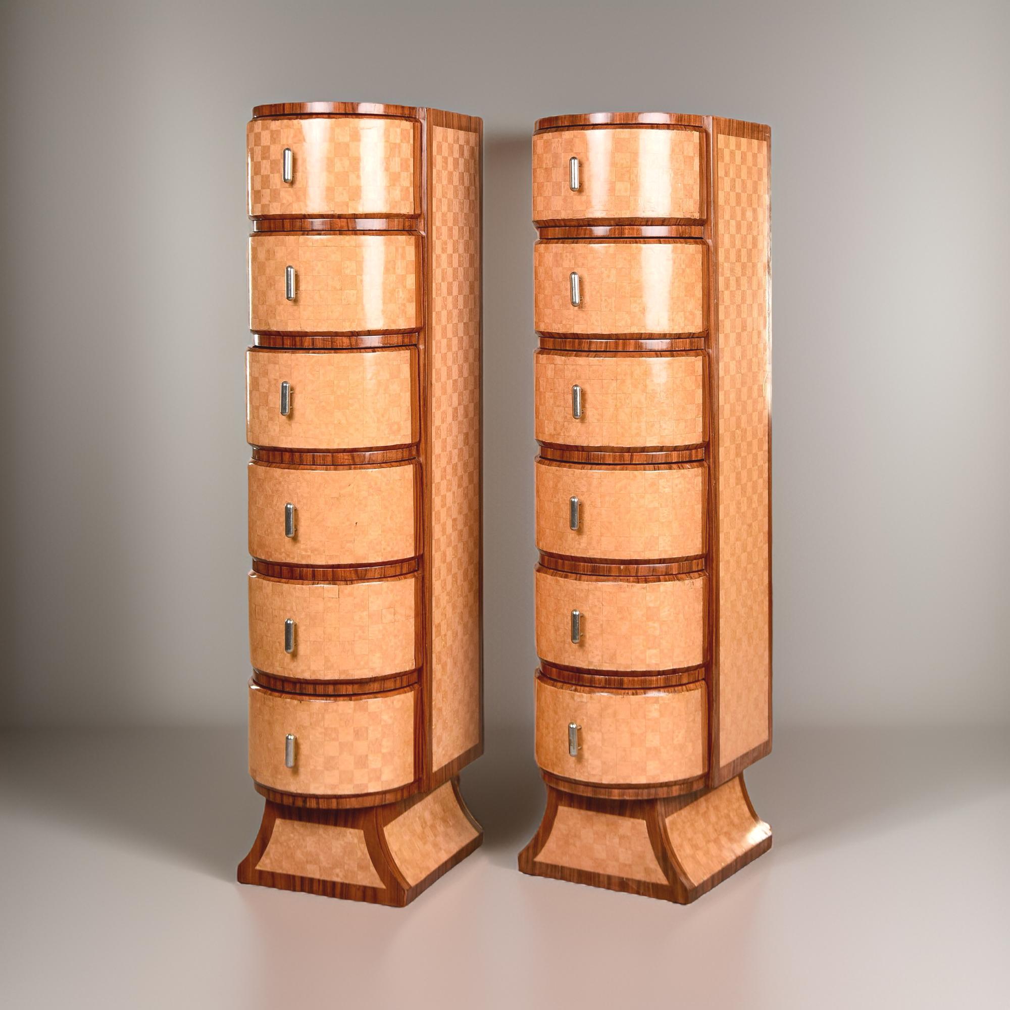 Found in Italy, this pair of tall, slender chests of drawers dates from the 1940s. The pair features satinwood veneers in a checked pattern with contrasting trim in a darker mahogany.  The chests stand 64” tall and have a pedestal base and six