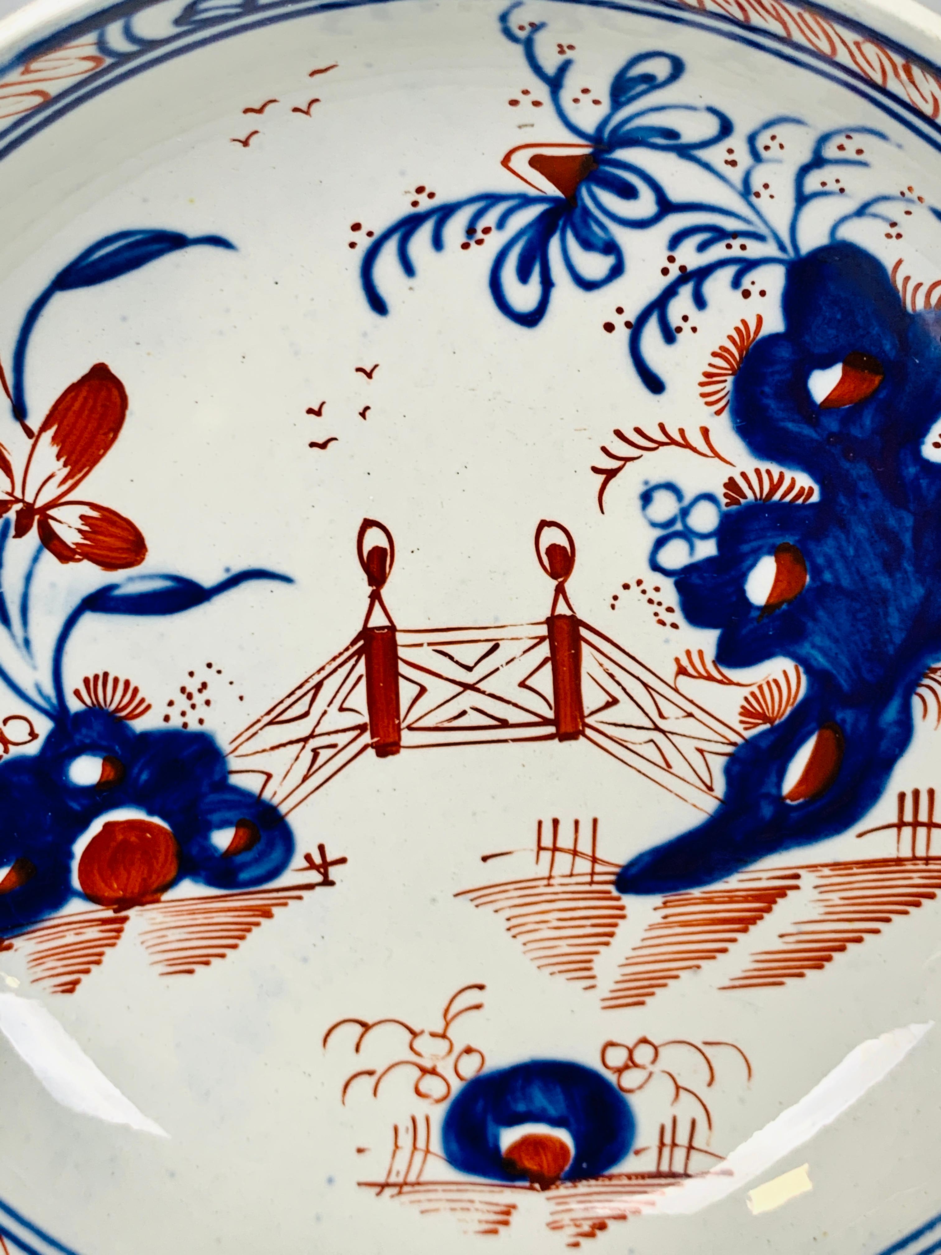 This is a lovely pair of hand-painted 18th century pearled creamware tea bowls and saucers. Made in England circa 1785, the cups and saucers are painted in a chinoiserie pattern with Imari colors. We see a garden with an oversized flower and two
