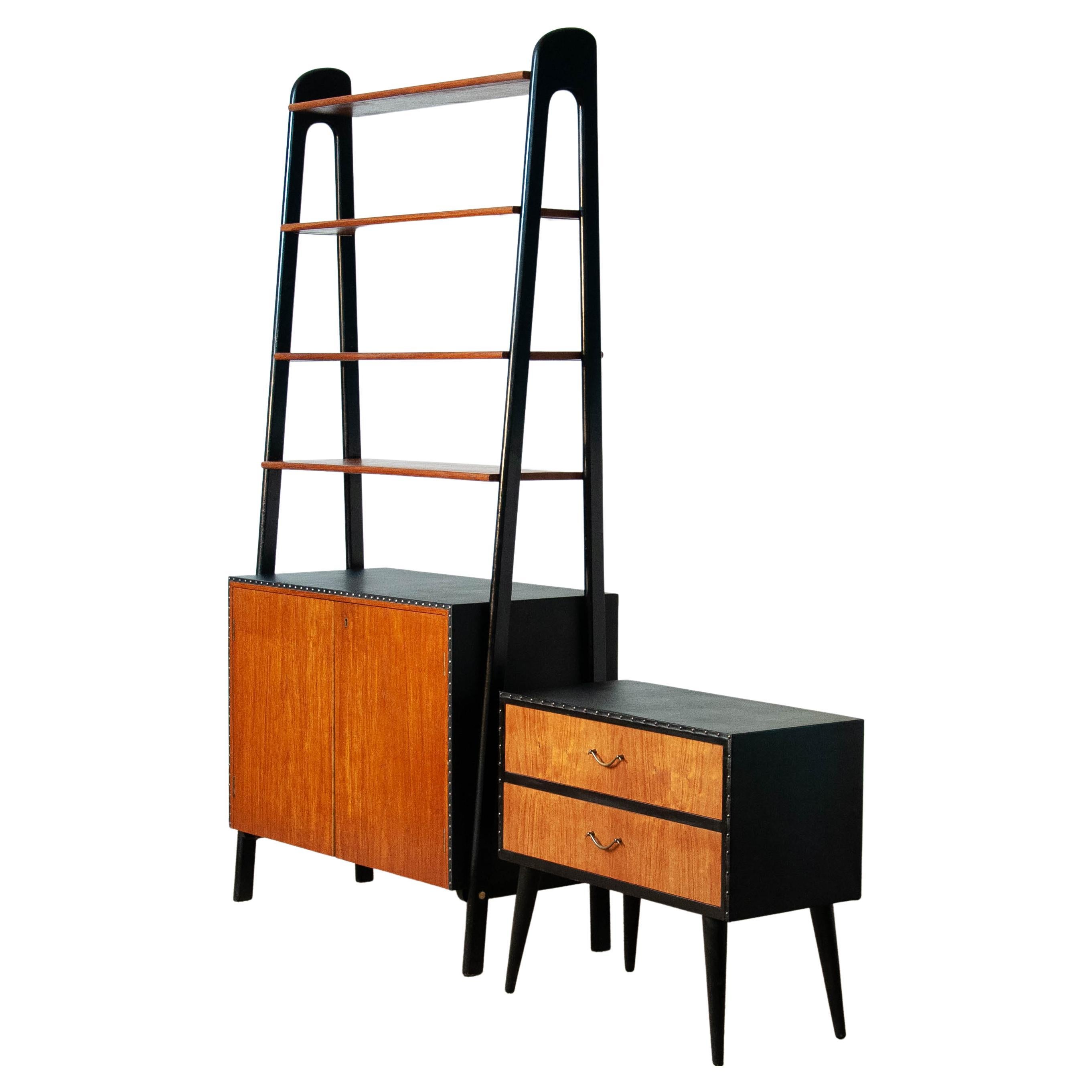 Beautiful set of a bookcase in teak and black faux leather, nailed, and black stands and a similar two drawer cabinet. On top the cabinet has four teak veneered shelfs. The two centered shelfs are adjustable in height. All four shelfs are made to