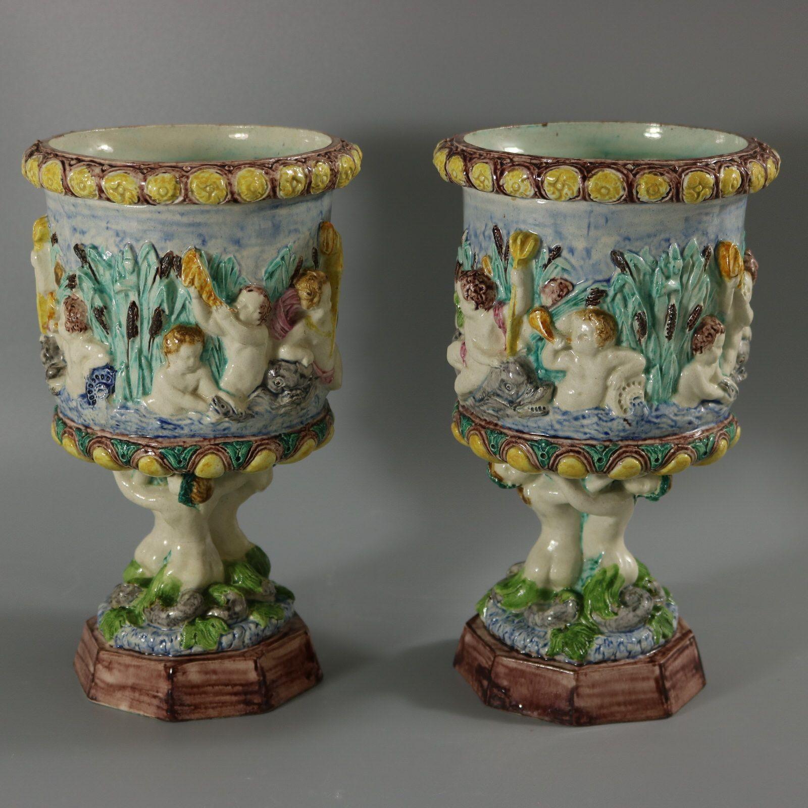 Pair of Thomas Sergent Majolica vases with a mythological theme which feature a river scene around the sides, with putti, dolphins, reeds and shells. The base stem in the form of merboys holding up the vessel. Colouration: blue, green, yellow, are