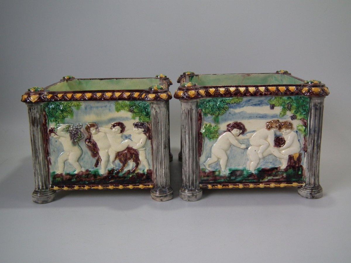 Pair of Thomas Sergent Palissy-style Majolica planters with a mythological theme which feature playful scenes of putti picking grapes. Columns on the corners. Coloration: Grey, cream, brown, are predominant. The piece bears maker's marks for the