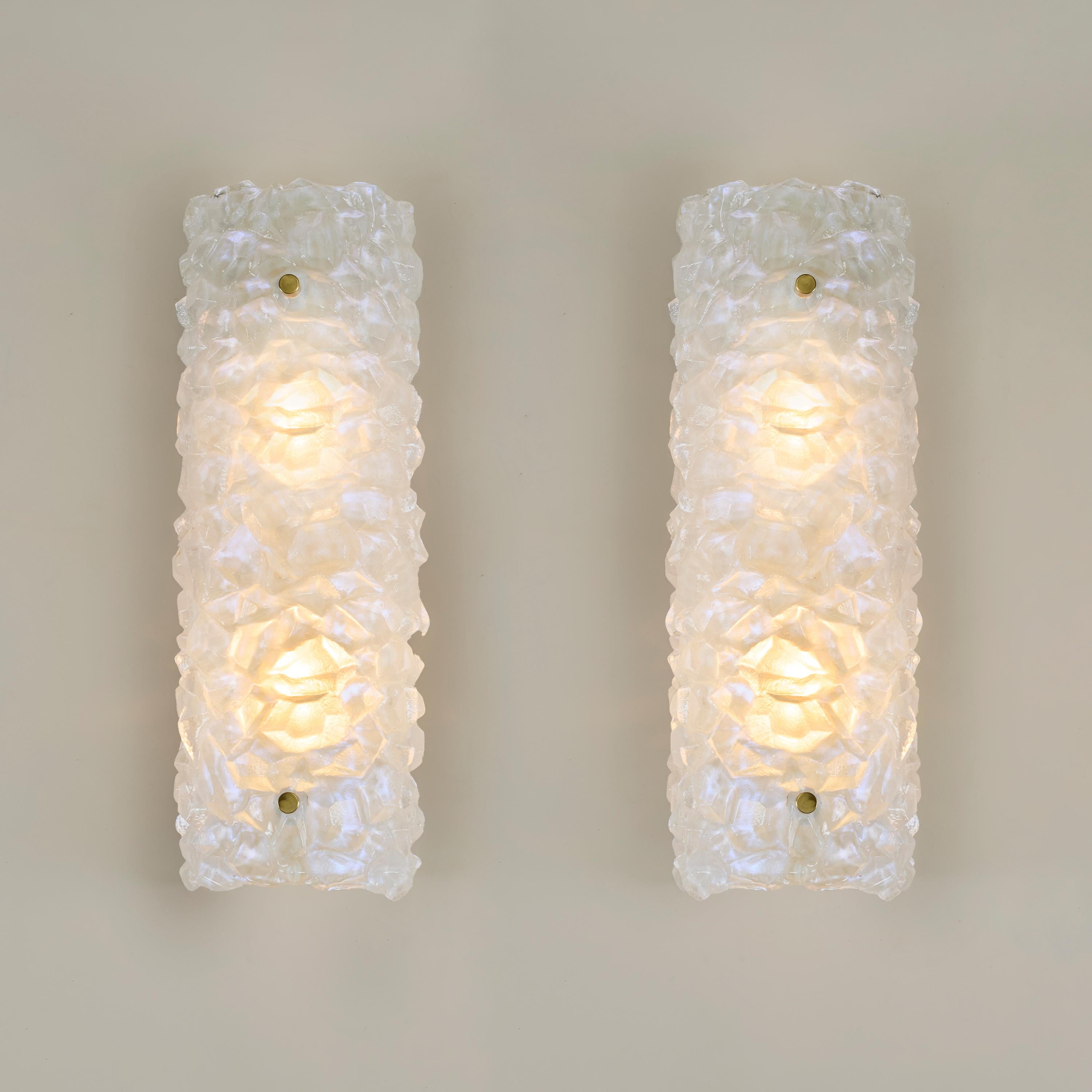 Sustancial e imponente pareja de apliques altos de Murano en grueso cristal opaco  con un sutil acabado iridiscente. Al estilo de Mazzega, el cristal forma un dibujo irregular similar al hielo. Cada lámpara tiene dos remates decorativos de latón y