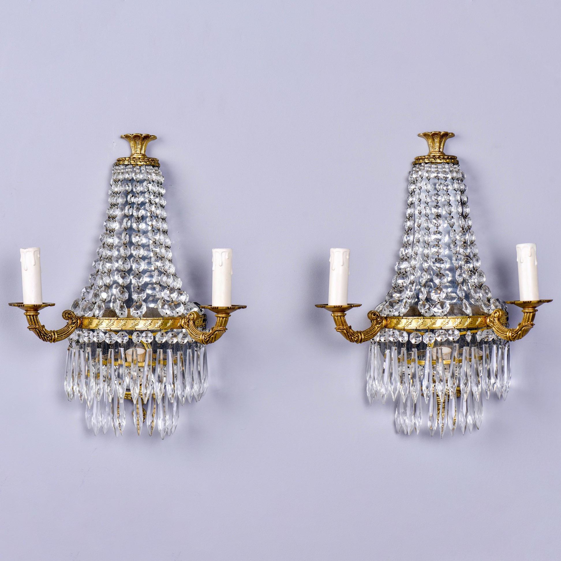 Found in England, this pair of circa 1940s two-light sconces feature a brass frame draped with crystal beading on the top level and two tiers of crystal pendants on the bottom. Unknown maker. New wiring for US electrical standards. Sold and priced