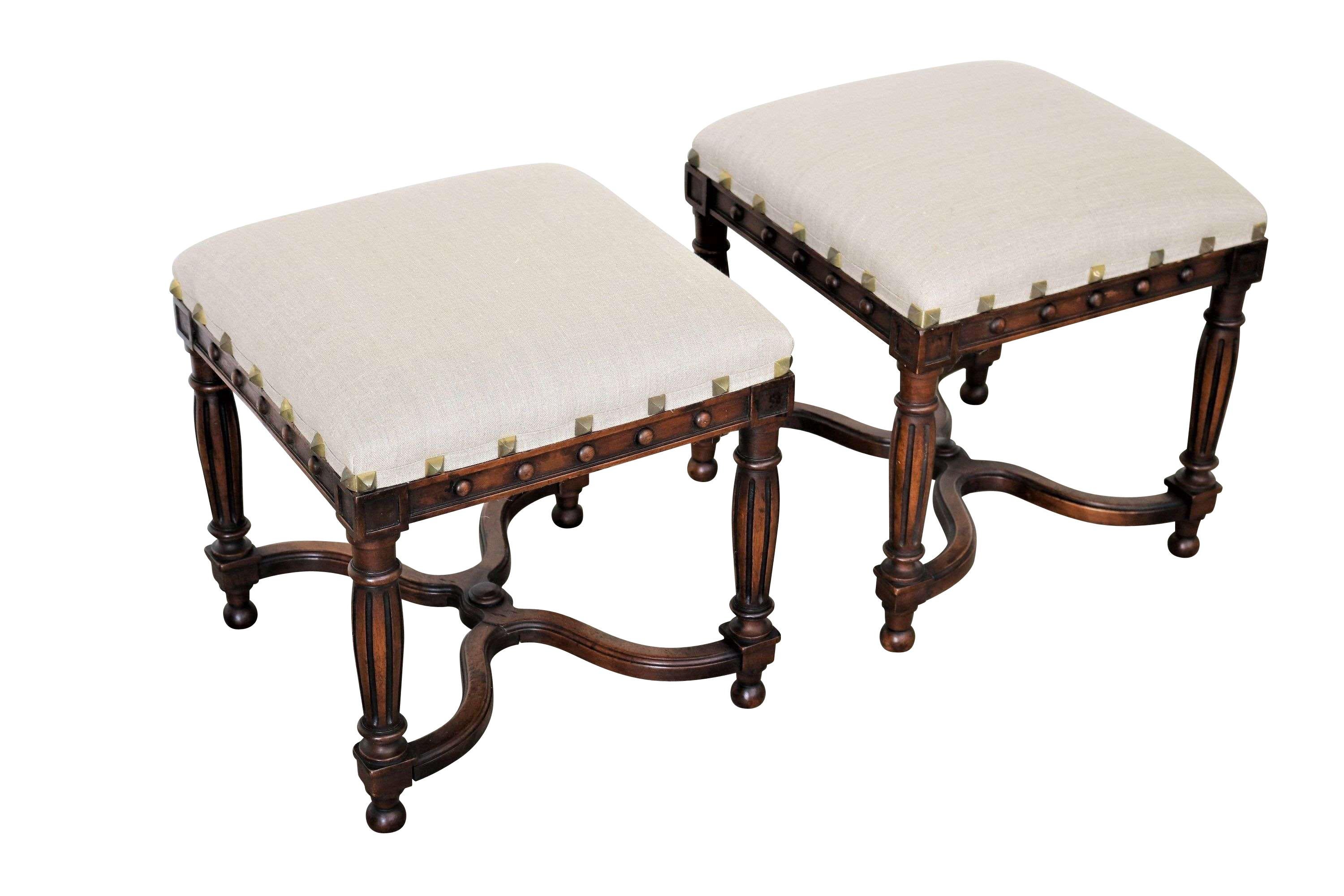 19th century English pair of upholstered walnut foot stools.
Decorative fluted legs.
Traditional X shaped stretcher at bottom.
Newly reupholstered in Belgian linen.
Decorative large brass tacking around apron.
 