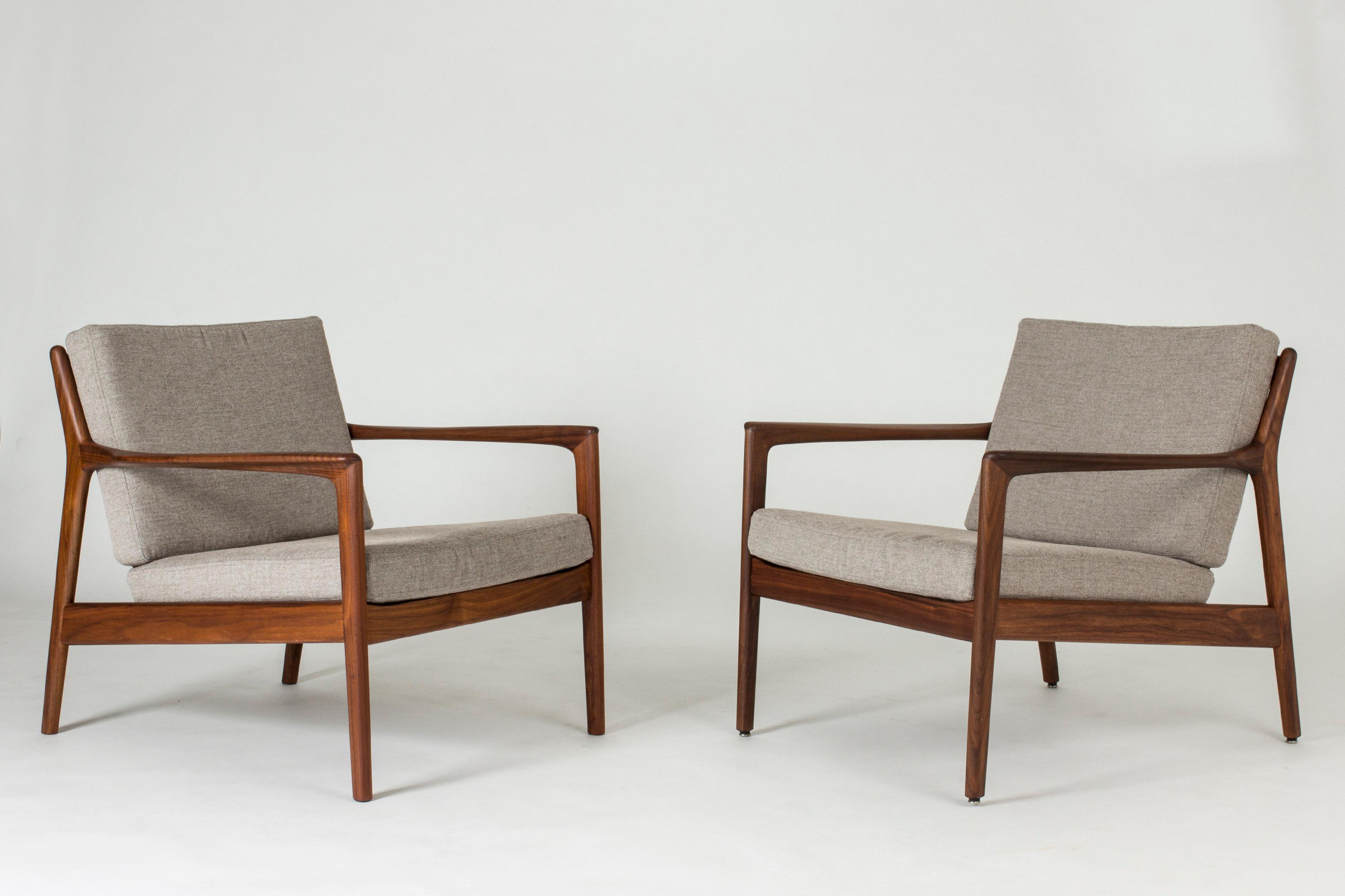 Pair of elegant and comfortable “USA 75” teak lounge chairs by Folke Ohlsson, with loose grey cushions. Beautifully sculpted armrests and ribbing in the back.
 