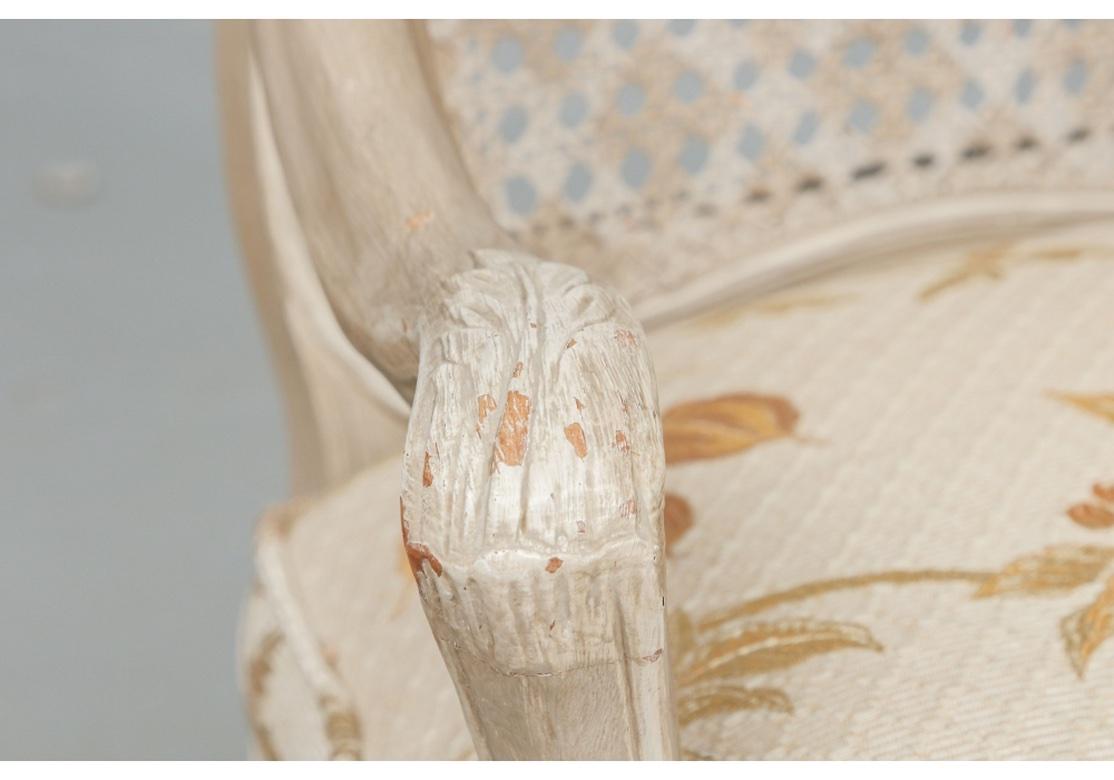 Style Louis XV en peinture taupe pâle avec des détails sculptés peints en blanc et un dossier et une assise cannés peints. Avec des détails feuillagés classiques et des pieds cabriole en forme de X. Avec des coussins d'assise confortables dans un