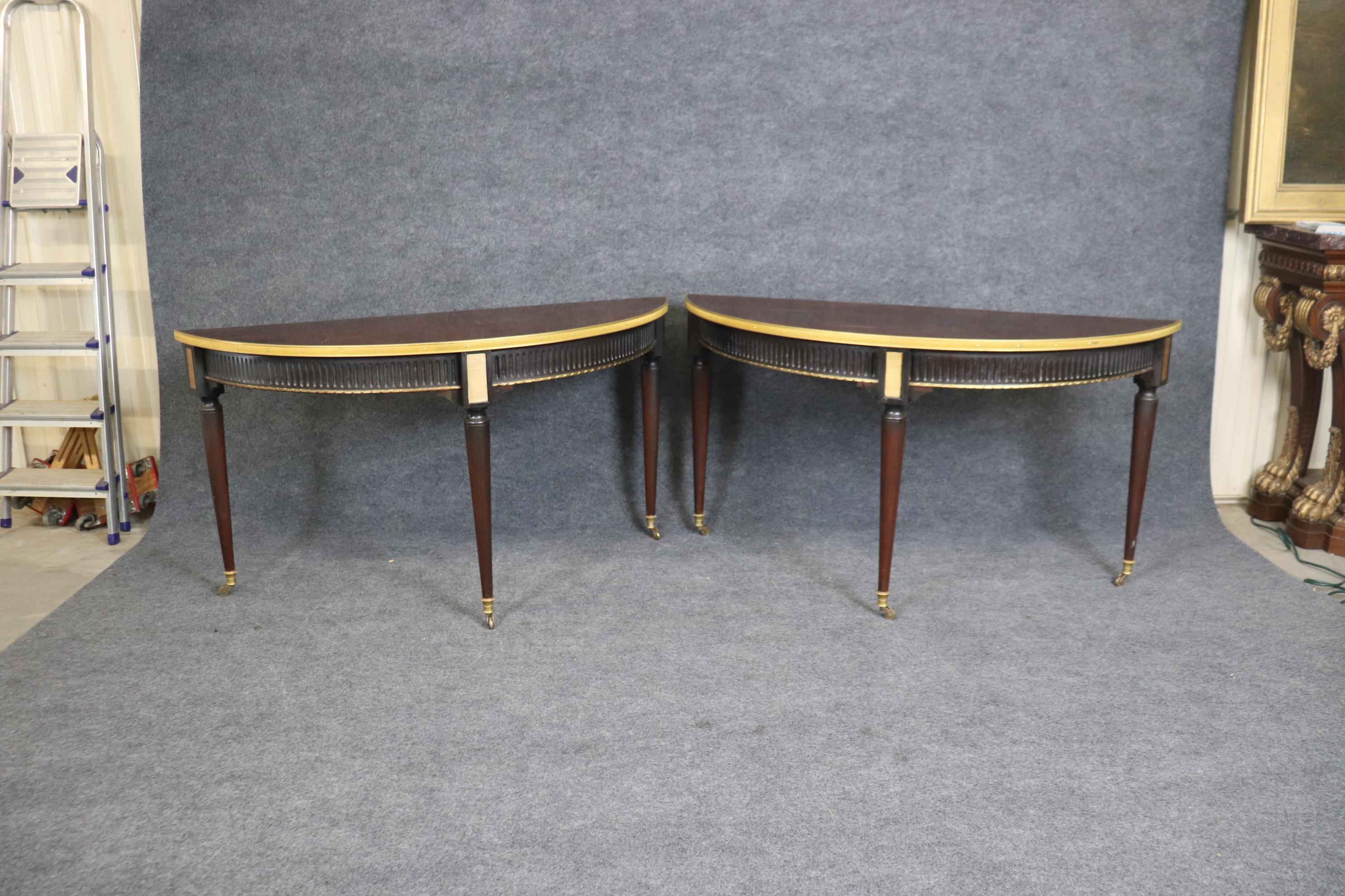 This is a gorgeous paid of beautiful mahogany and brass bound and ormolu demilune consoles. They each measures 58 wide x 22.25 deep x 31.25 tall. The tables are in good original condition with minor signs of age and wear due to normal age and use.